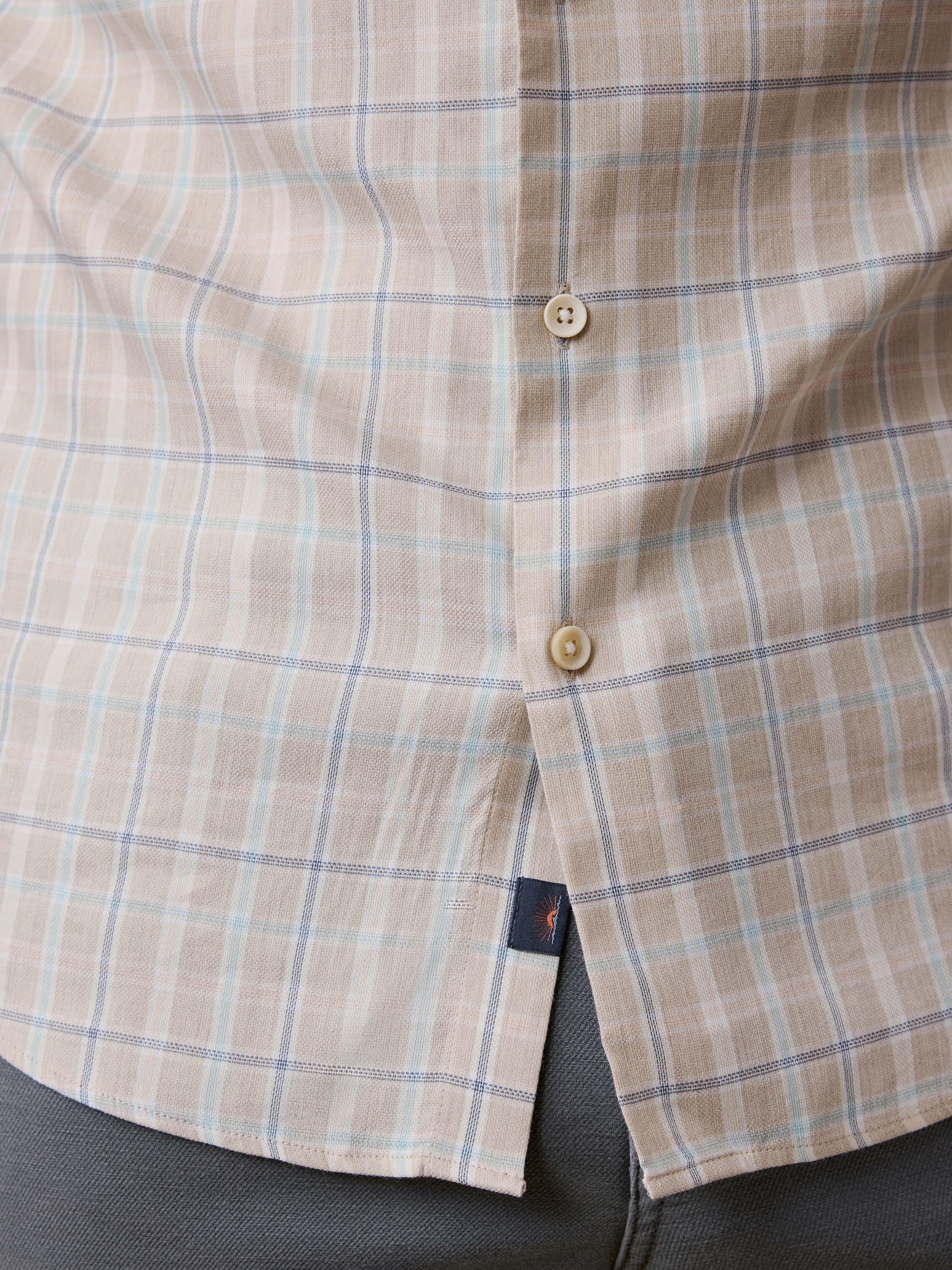 Close-up of a plaid shirt with a button and Faherty brand label at the hem
