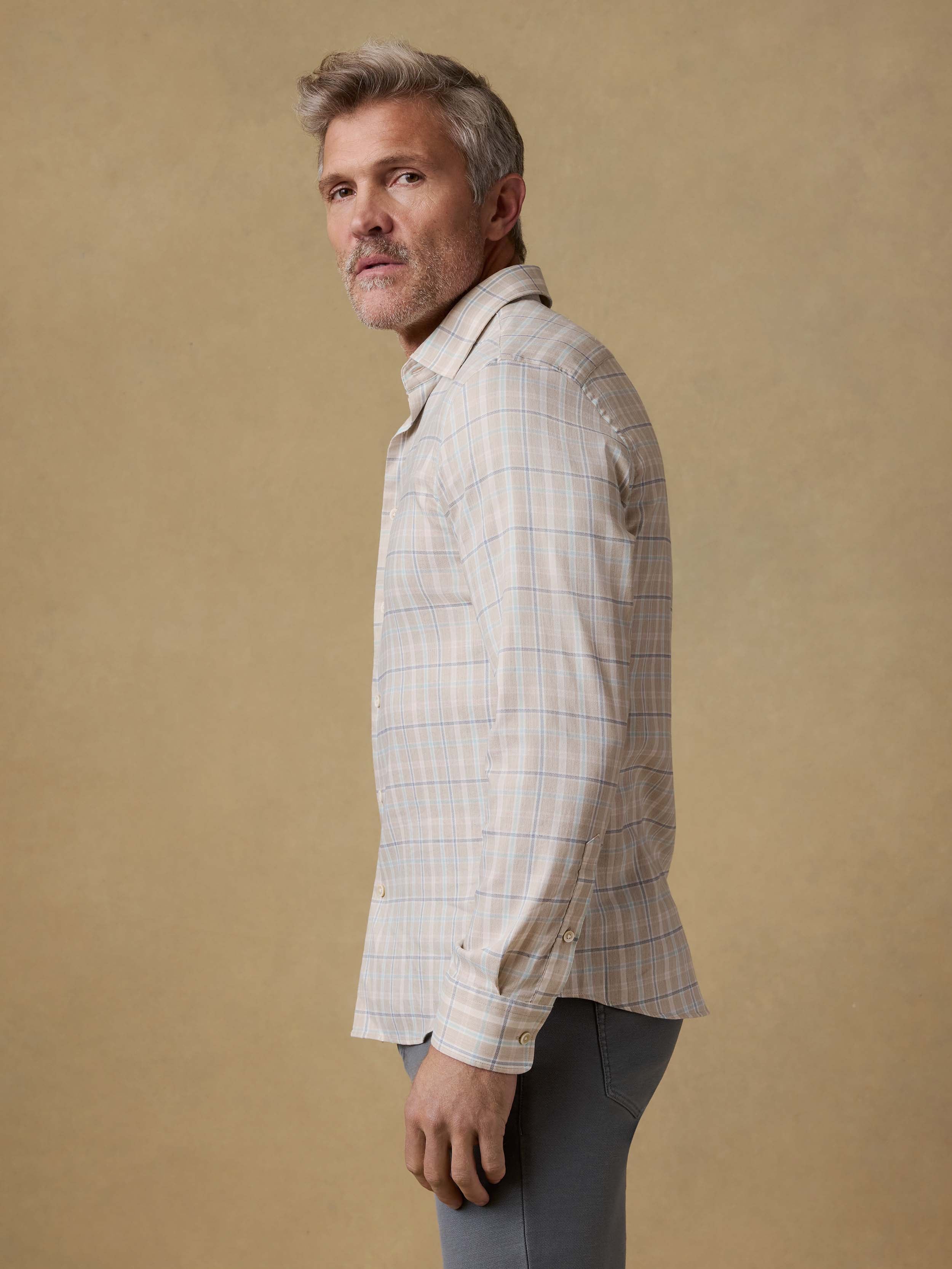 Man wearing a light-colored plaid shirt and grey pants against a beige background