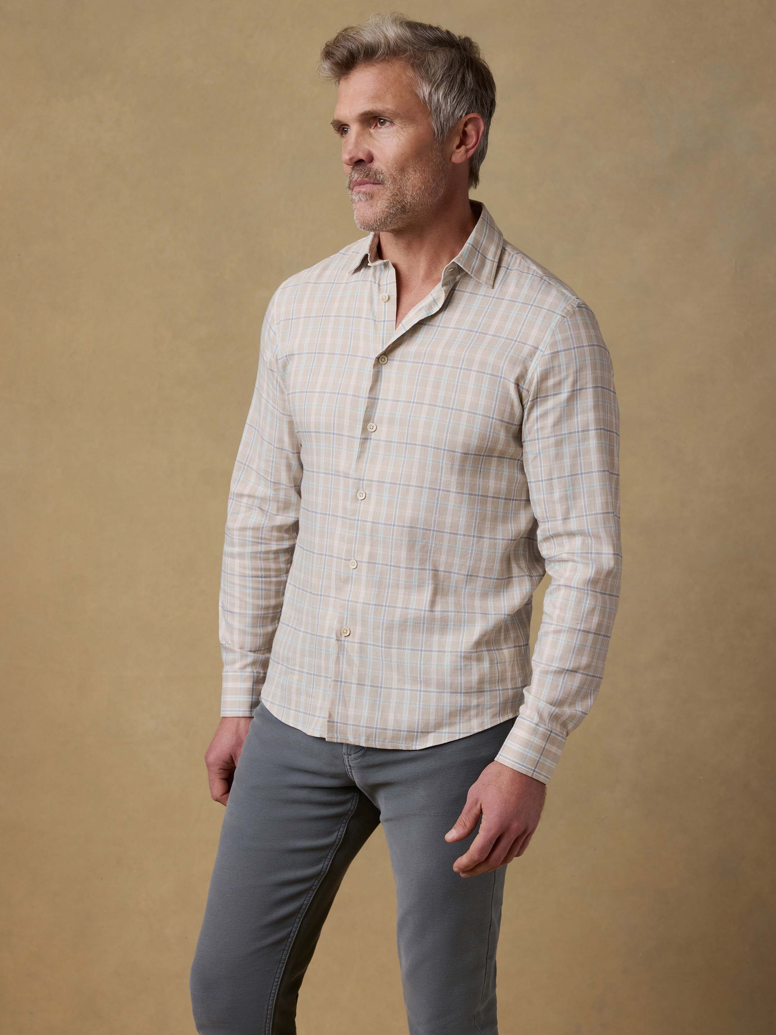 Man wearing a plaid shirt and gray pants against a beige background