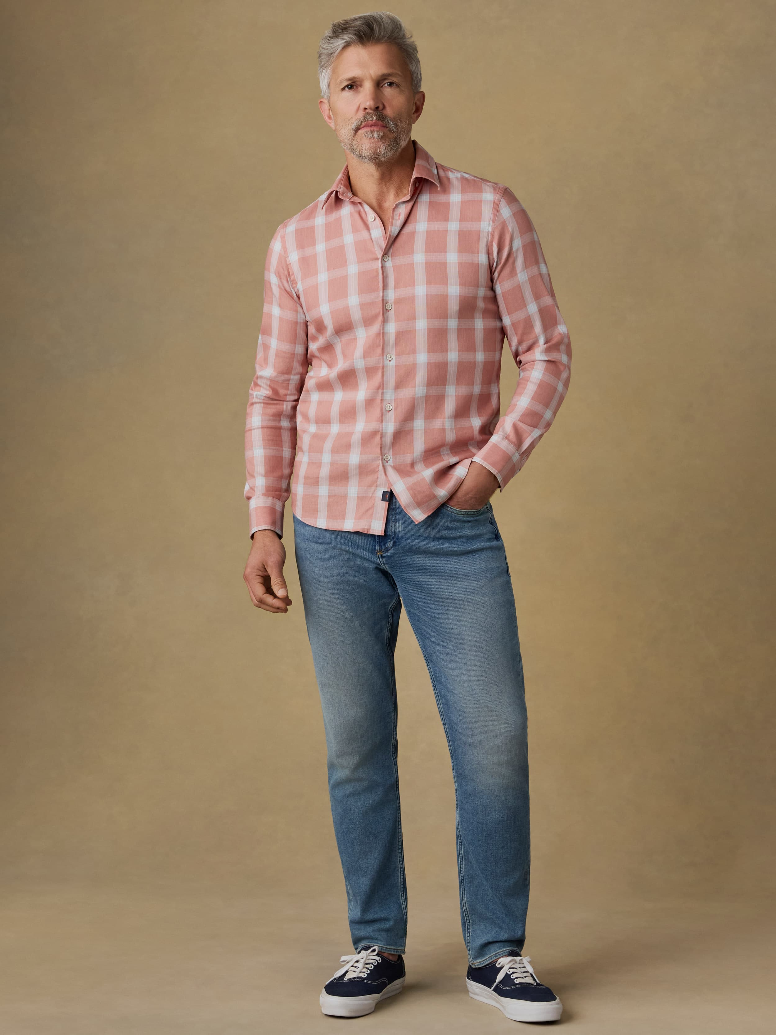 Man wearing a light red plaid shirt and blue jeans against a beige background