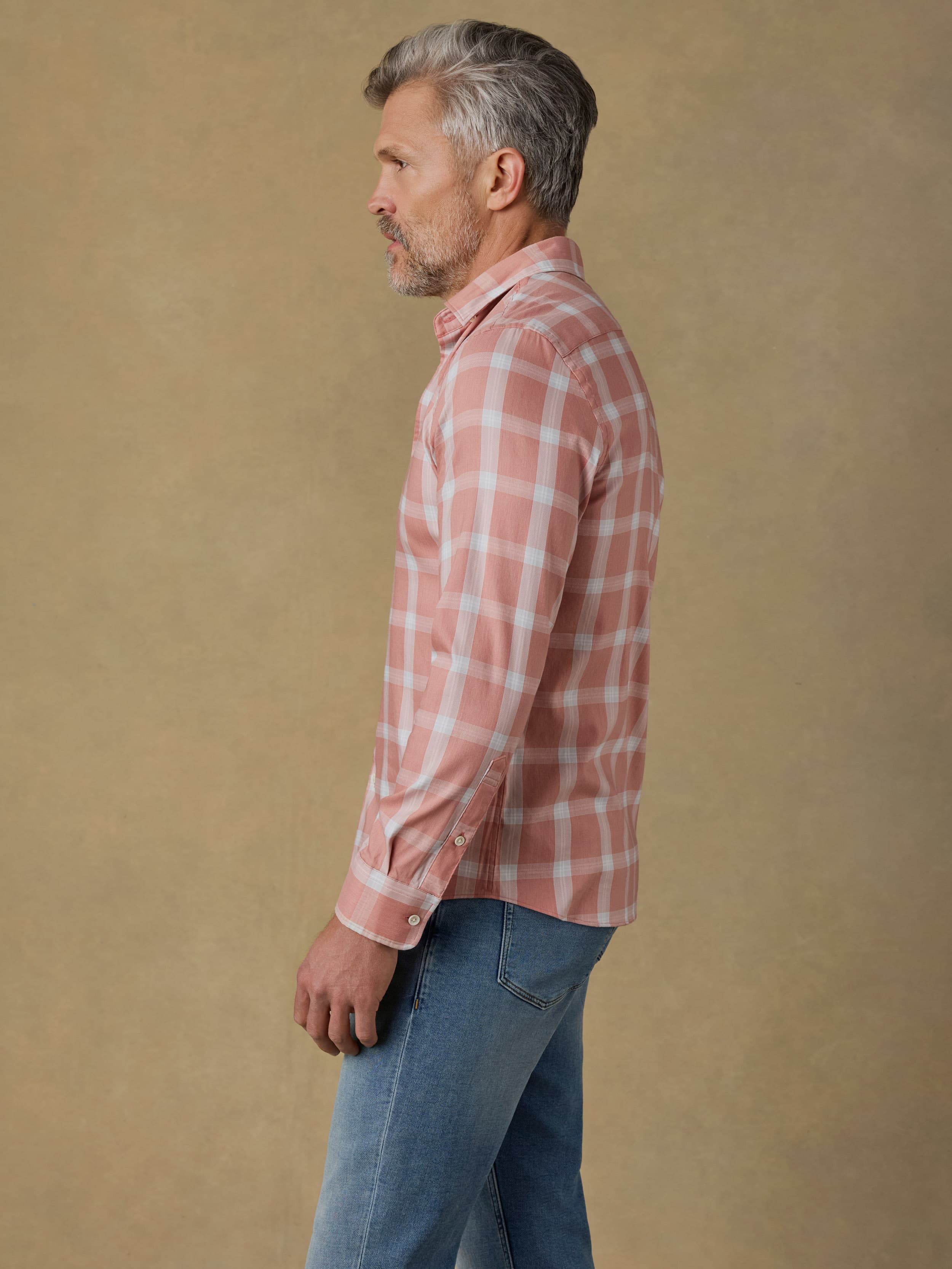 Man wearing a light red plaid shirt and blue jeans against a beige background