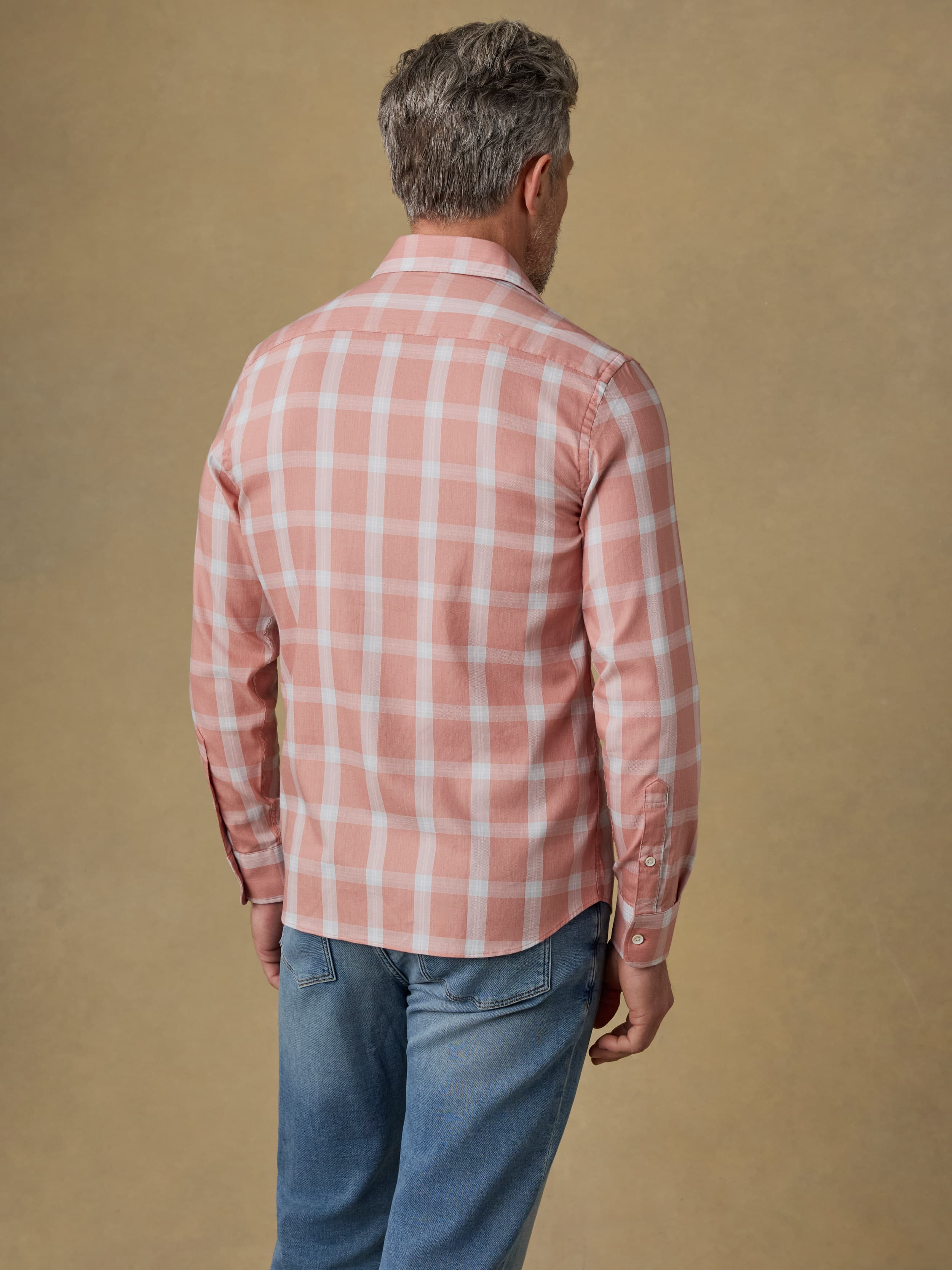 Man wearing a light red plaid shirt and blue jeans against a beige background