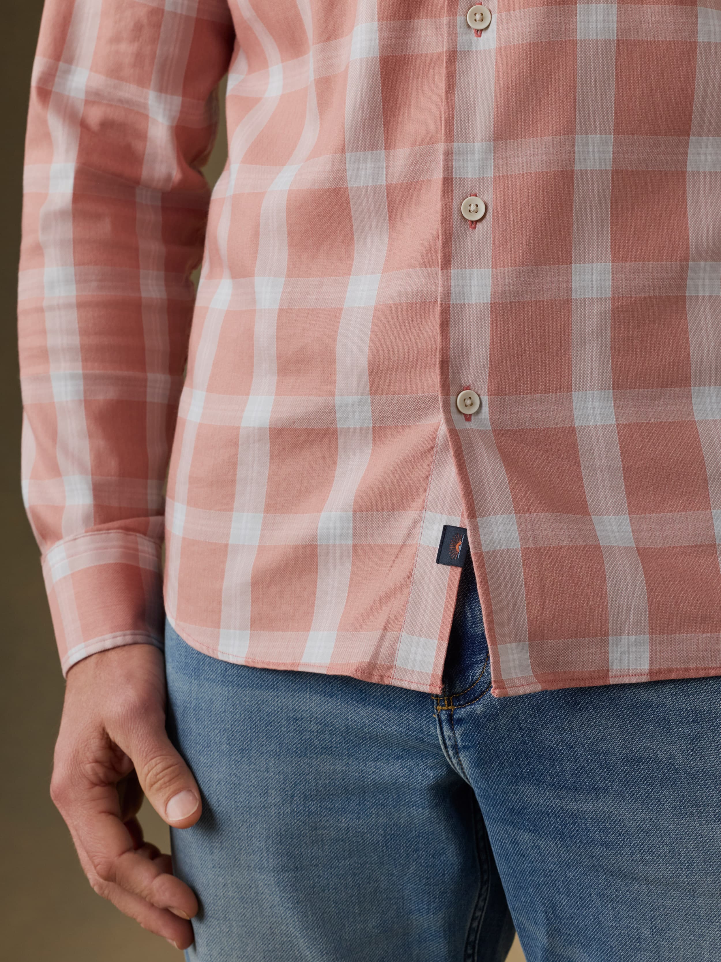 Man wearing a light red and white checkered shirt over blue jeans against a beige background
