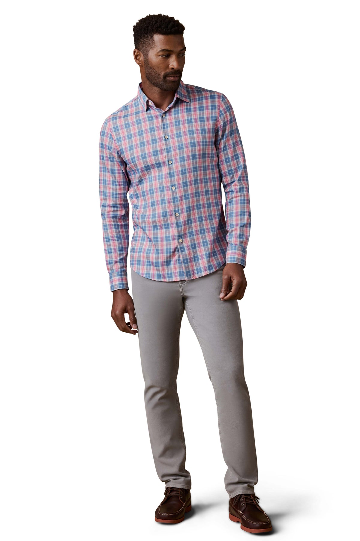 A man wearing a red and blue plaid shirt, grey pants, and brown shoes, image 2 of 3