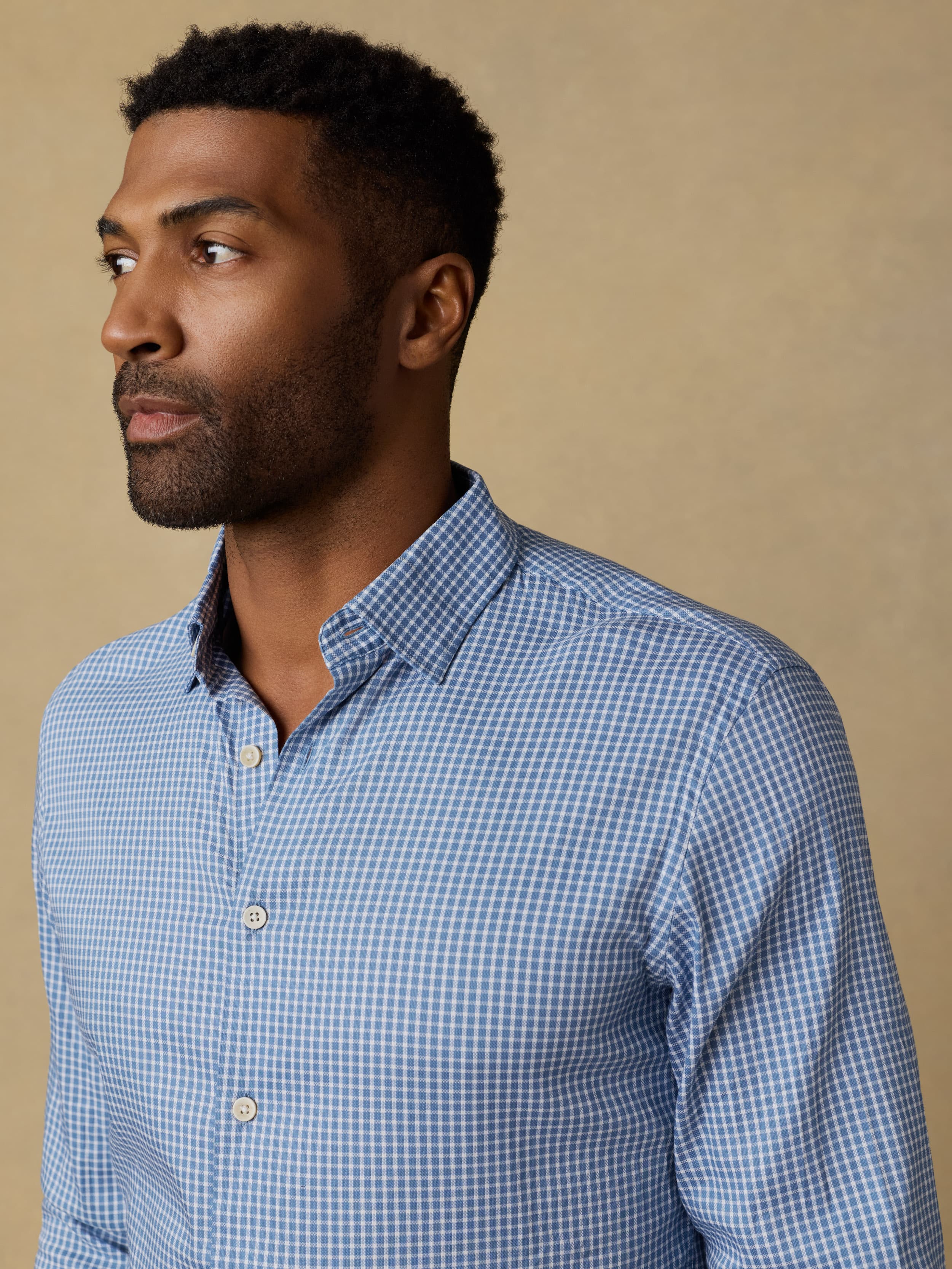 Man wearing a blue checkered long sleeve button up shirt against a beige background