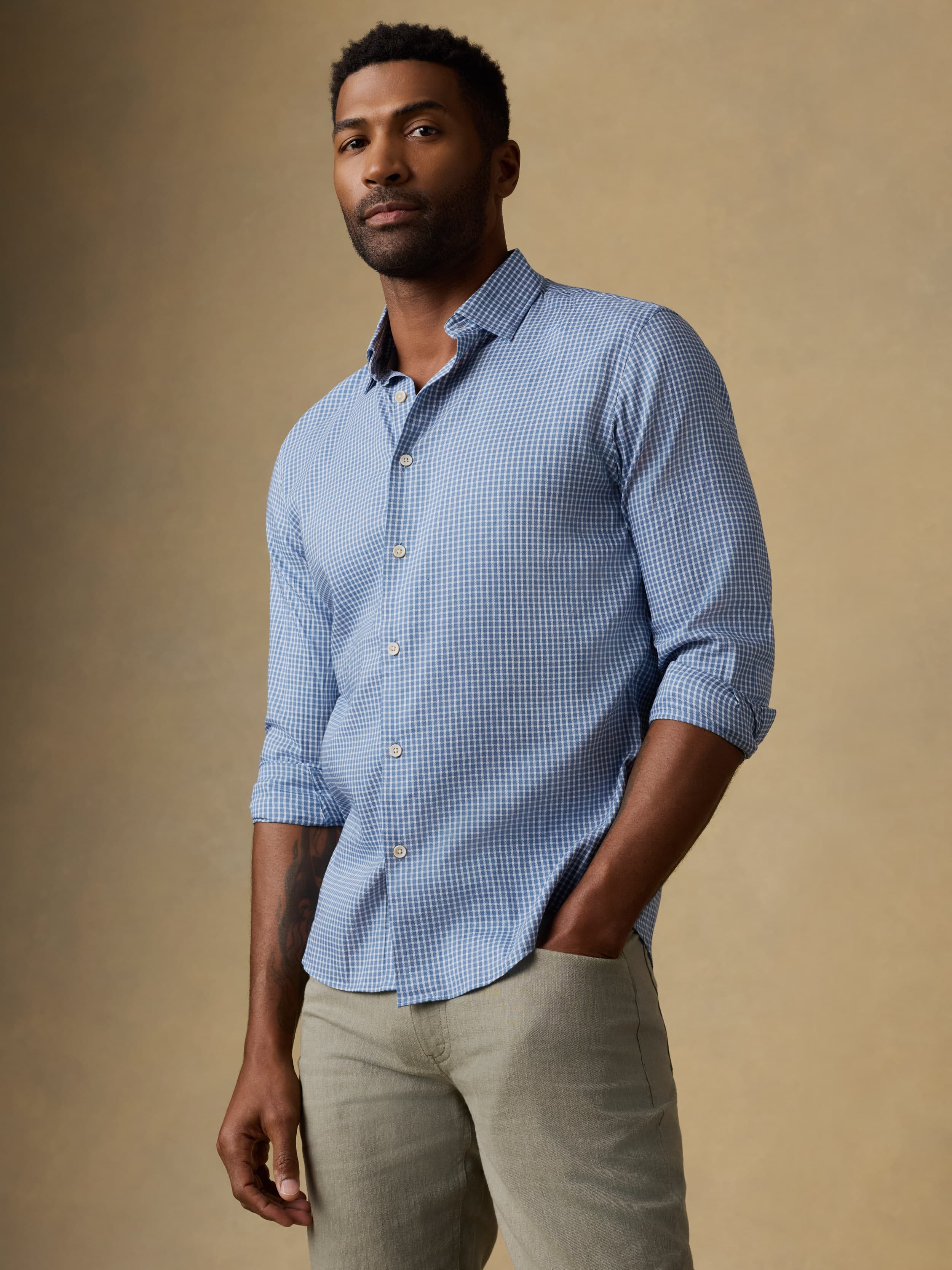 Man wearing a blue checkered long sleeve button up shirt and olive green pants against a beige background