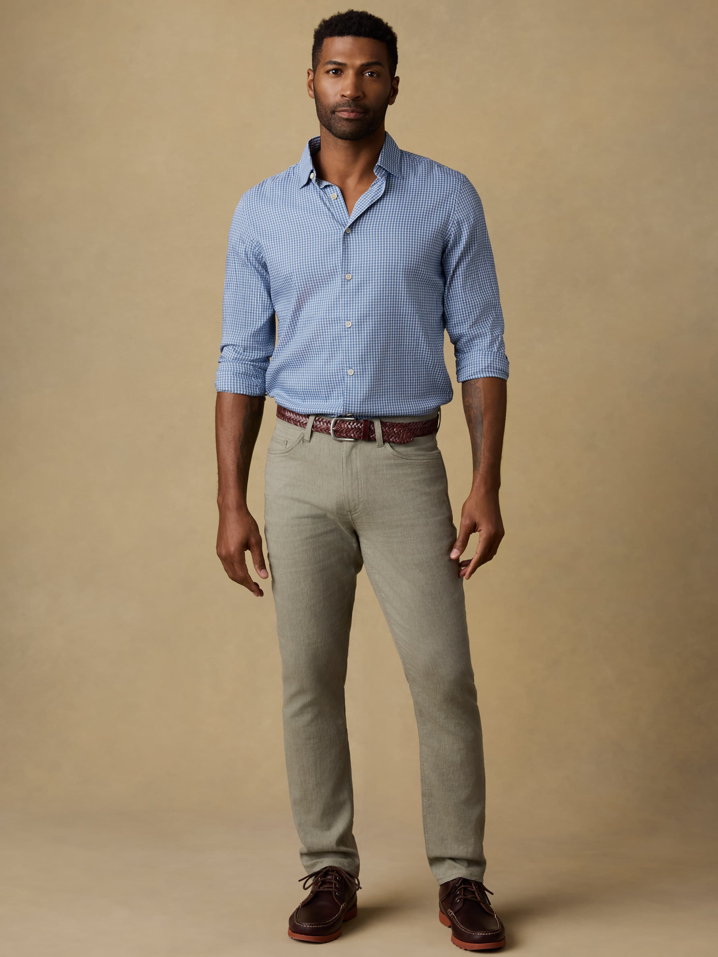 Man wearing a blue checkered long sleeve button up shirt and olive green pants against a beige background