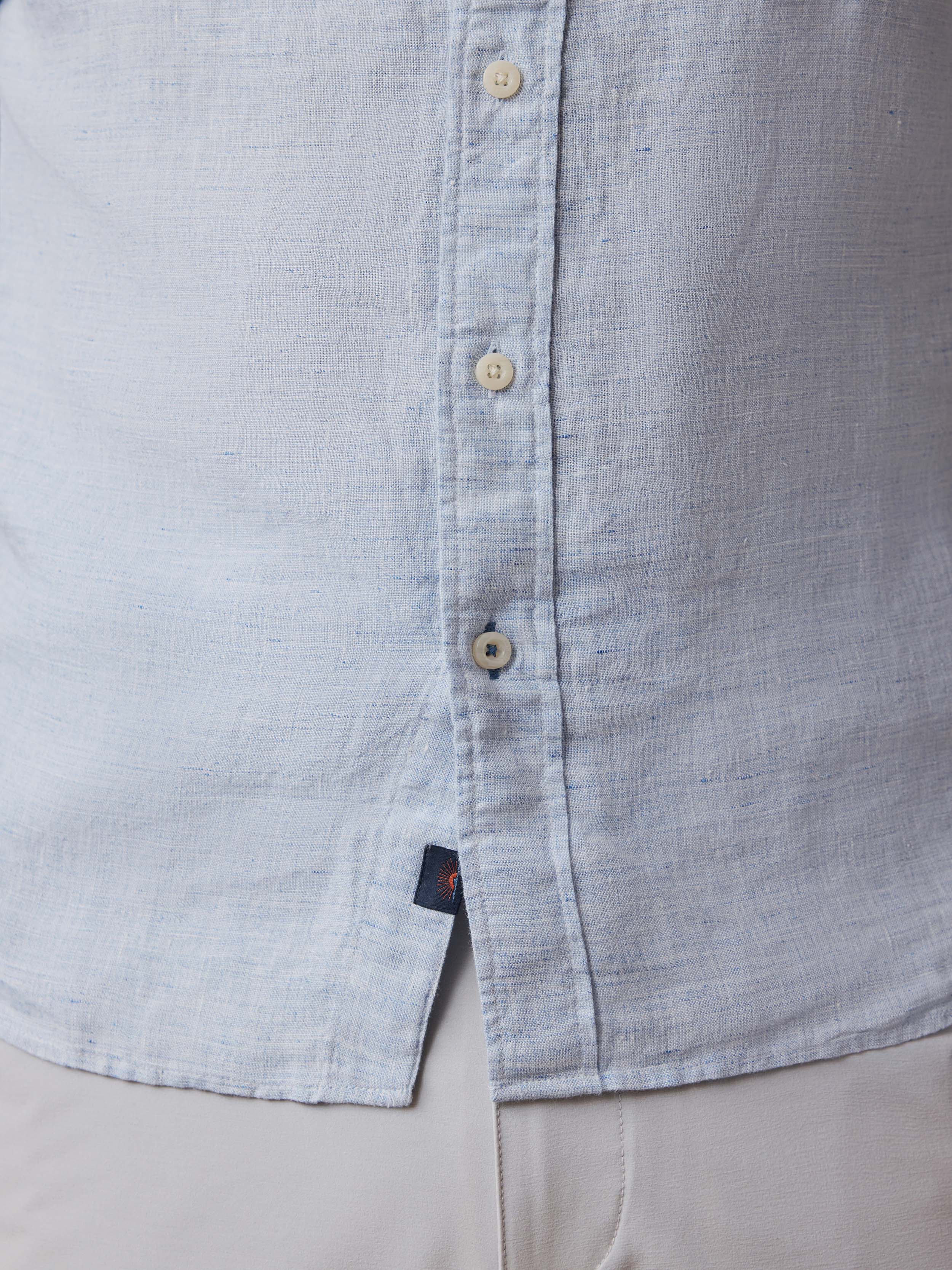 Close-up of a light blue button-up shirt with a Faherty brand label on a beige background