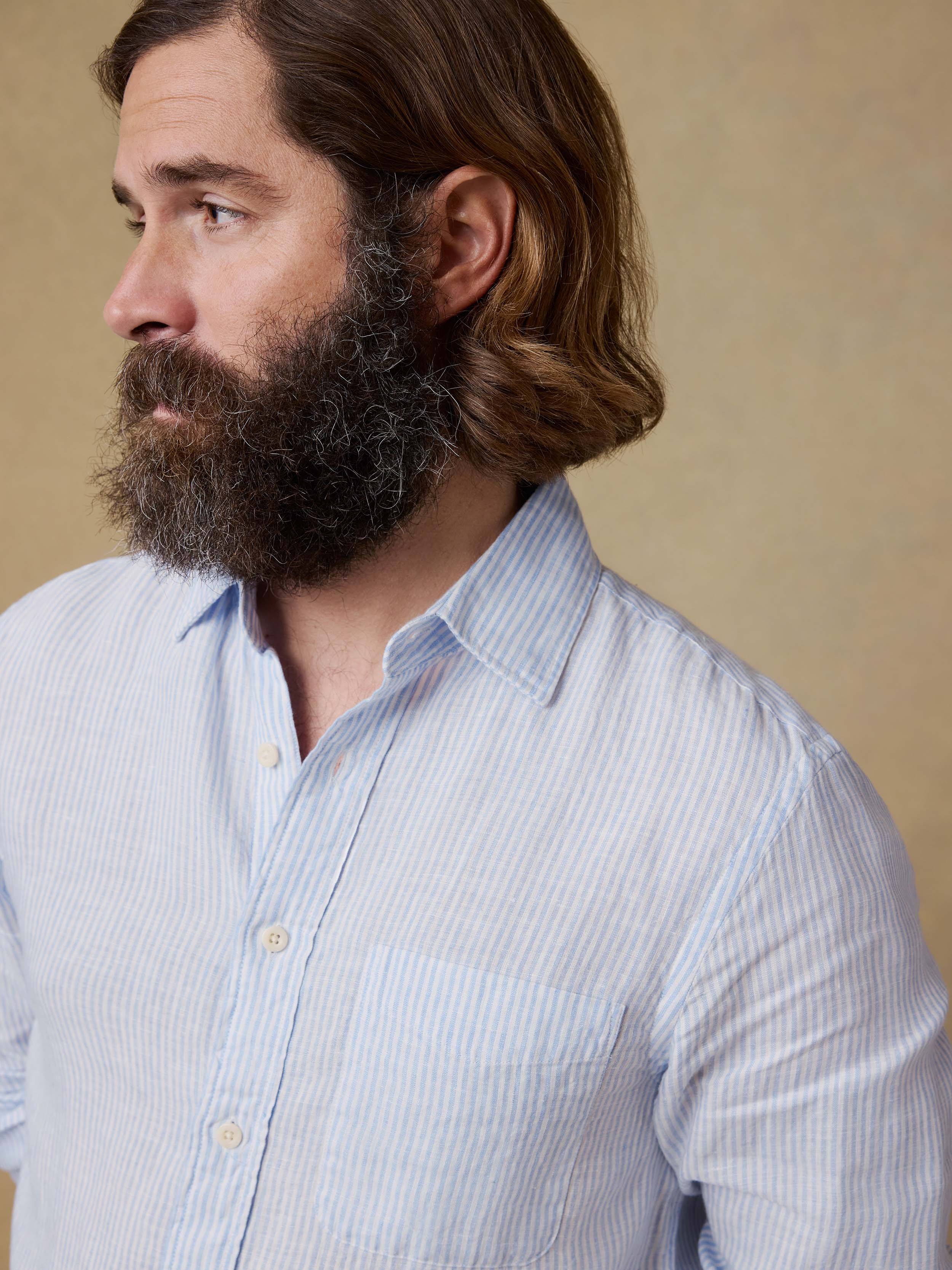 Man wearing a light blue striped button up shirt against a beige background
