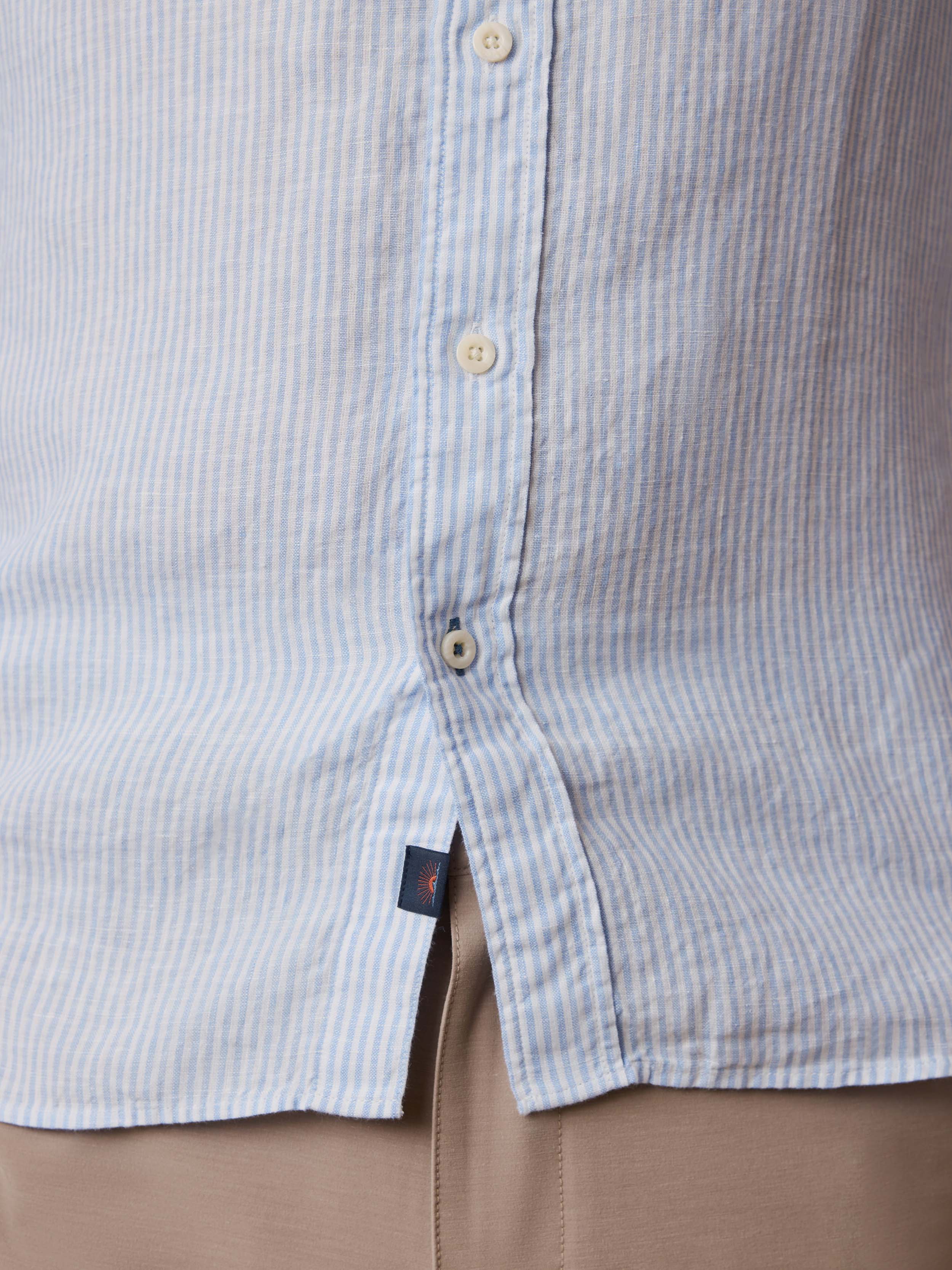 Close-up of a light blue striped button up shirt with a Faherty brand logo at the hem