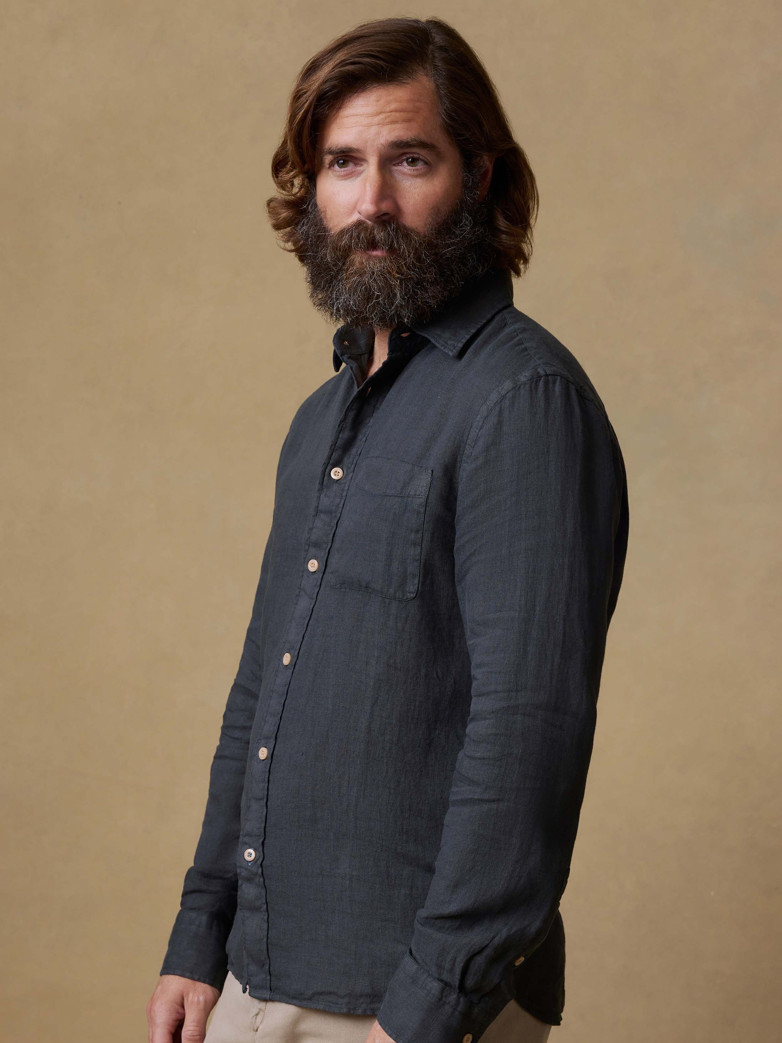 Man wearing a black button up shirt and beige pants against a beige background