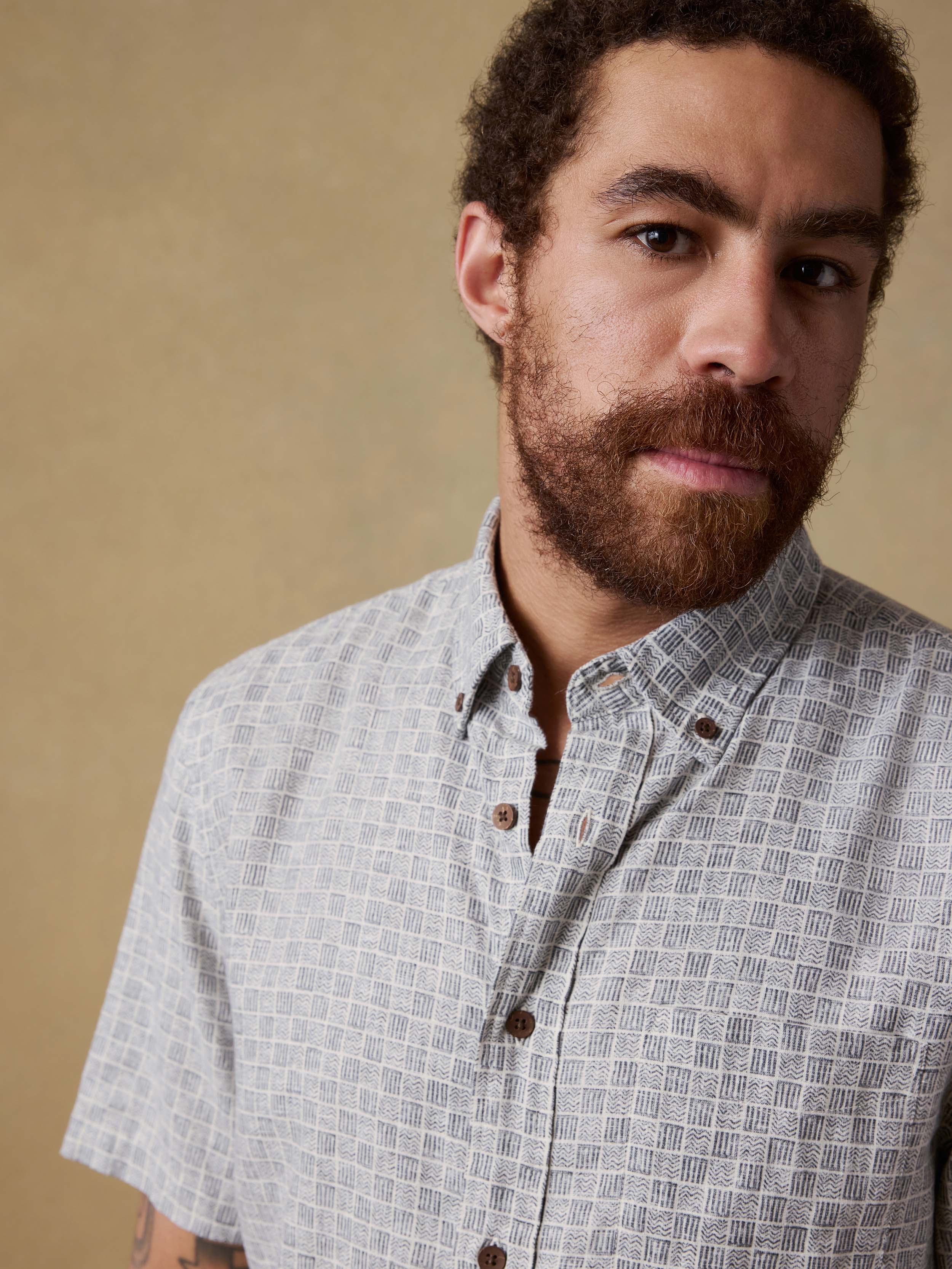 Detail shot of a man wearing a patterned short-sleeve shirt against a beige background