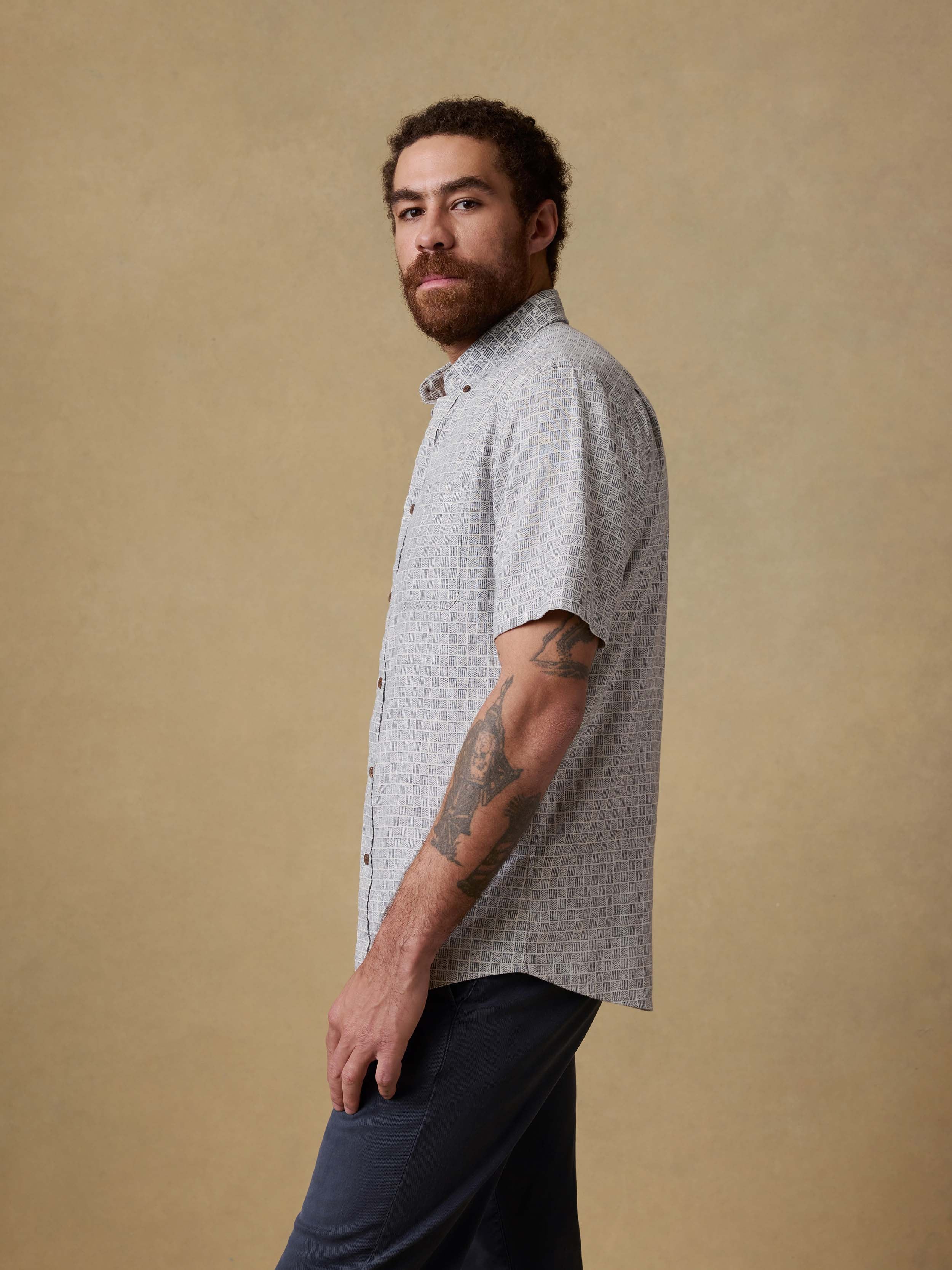 Man wearing a patterned short-sleeve shirt and navy pants against a beige background