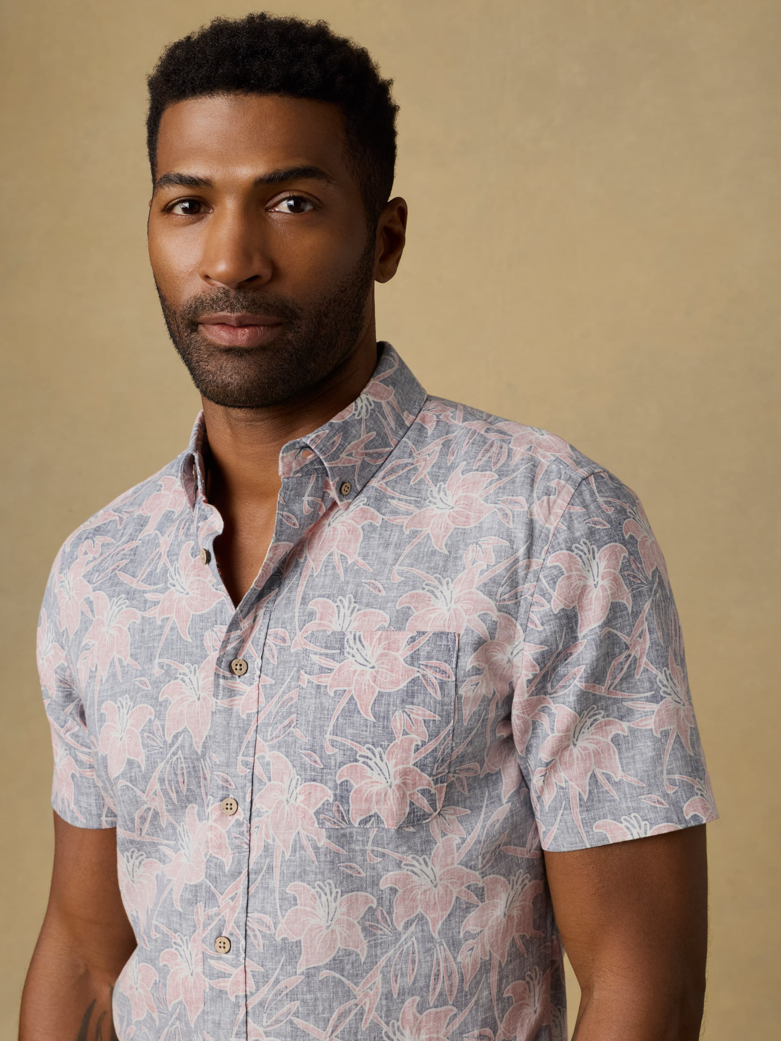 Man wearing a floral printed short sleeve button down shirt standing against a beige background