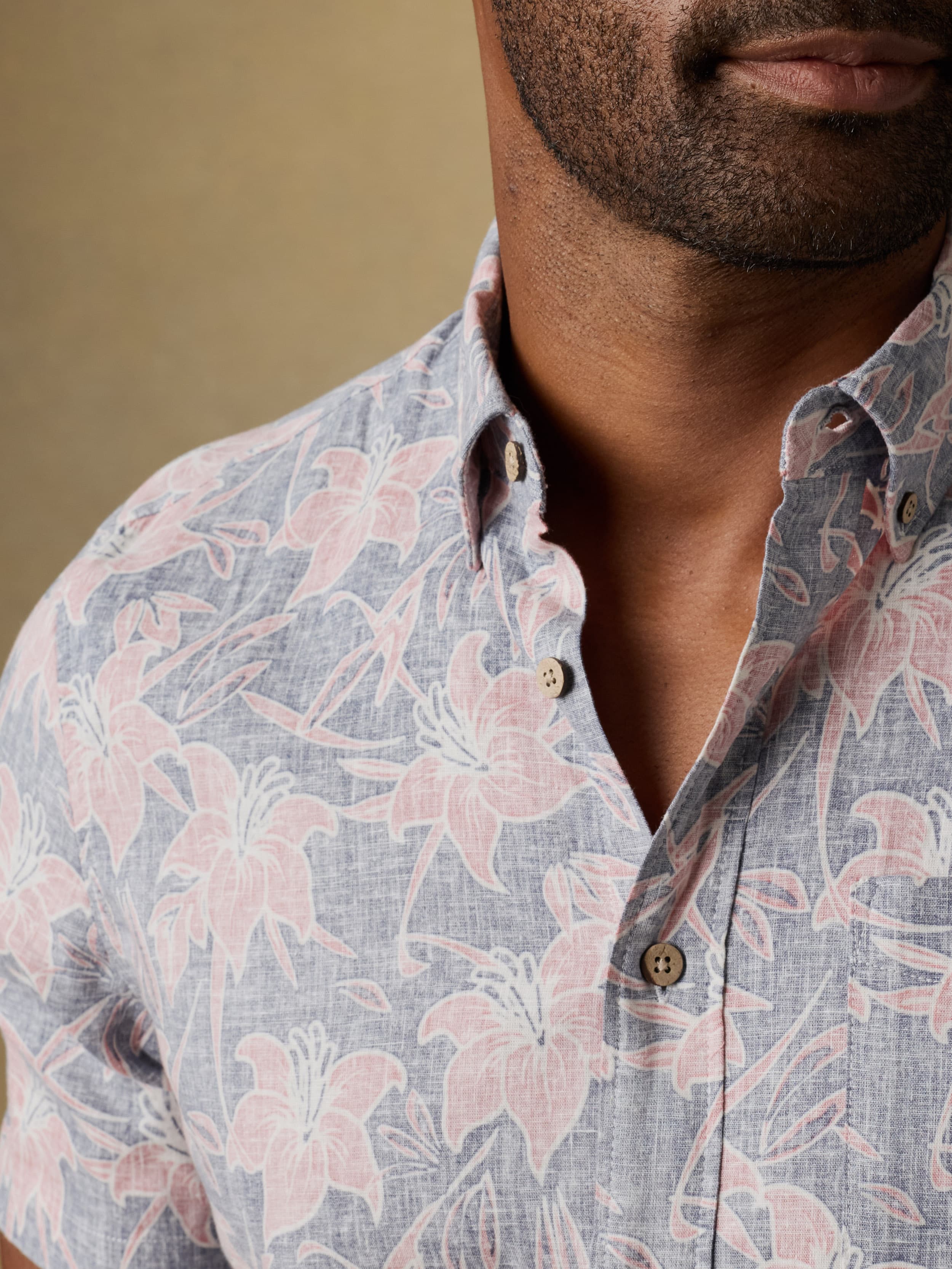 Close up shot of a man wearing a floral patterned short sleeve button down shirt against a beige background