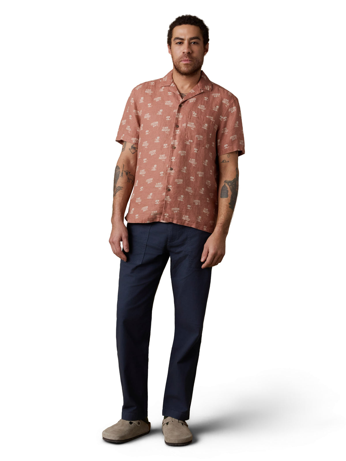 A man wearing a red button up shirt, blue pants, and birkenstocks, image 2 of 3