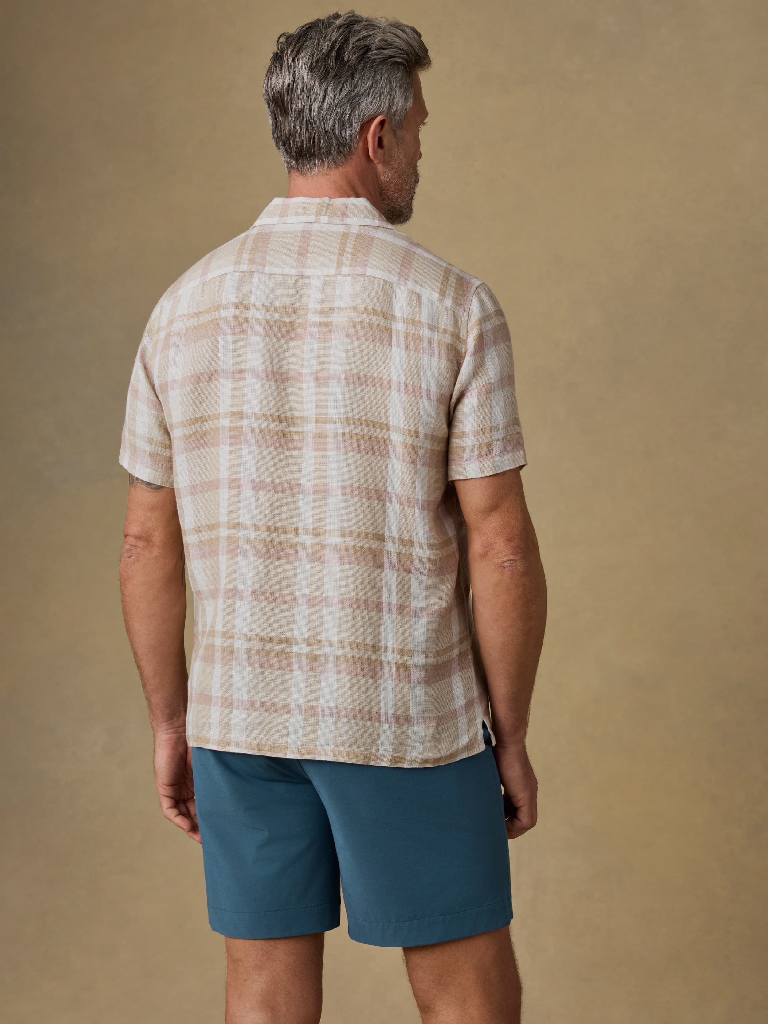 Man wearing a plaid shirt and blue shorts against a beige background