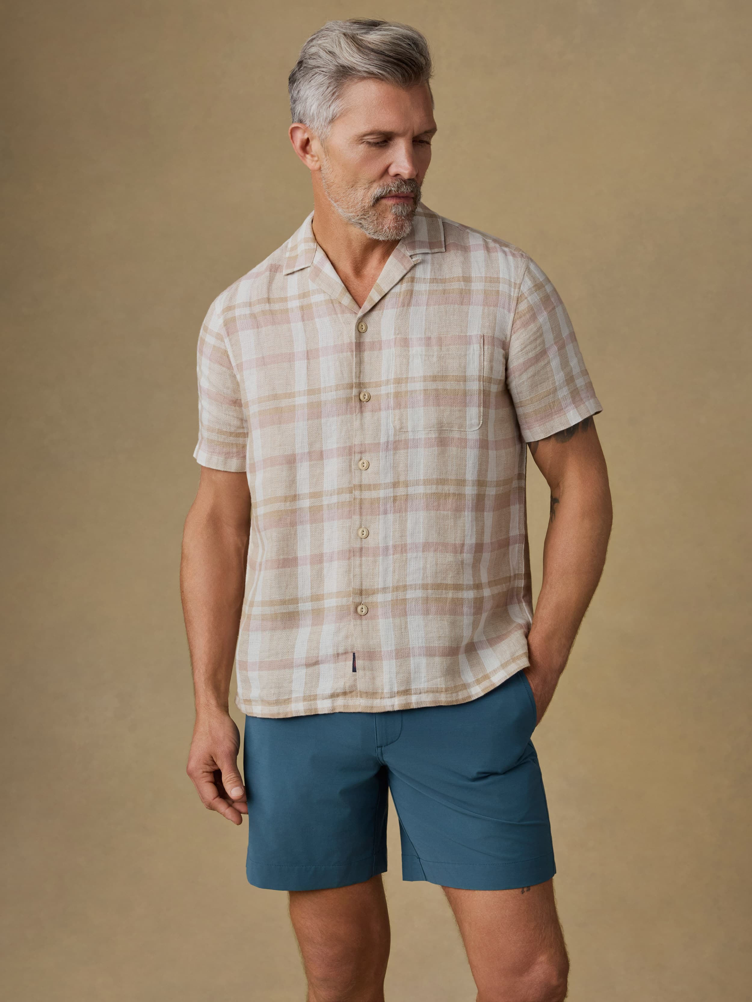 Man wearing a plaid shirt and blue shorts against a beige background
