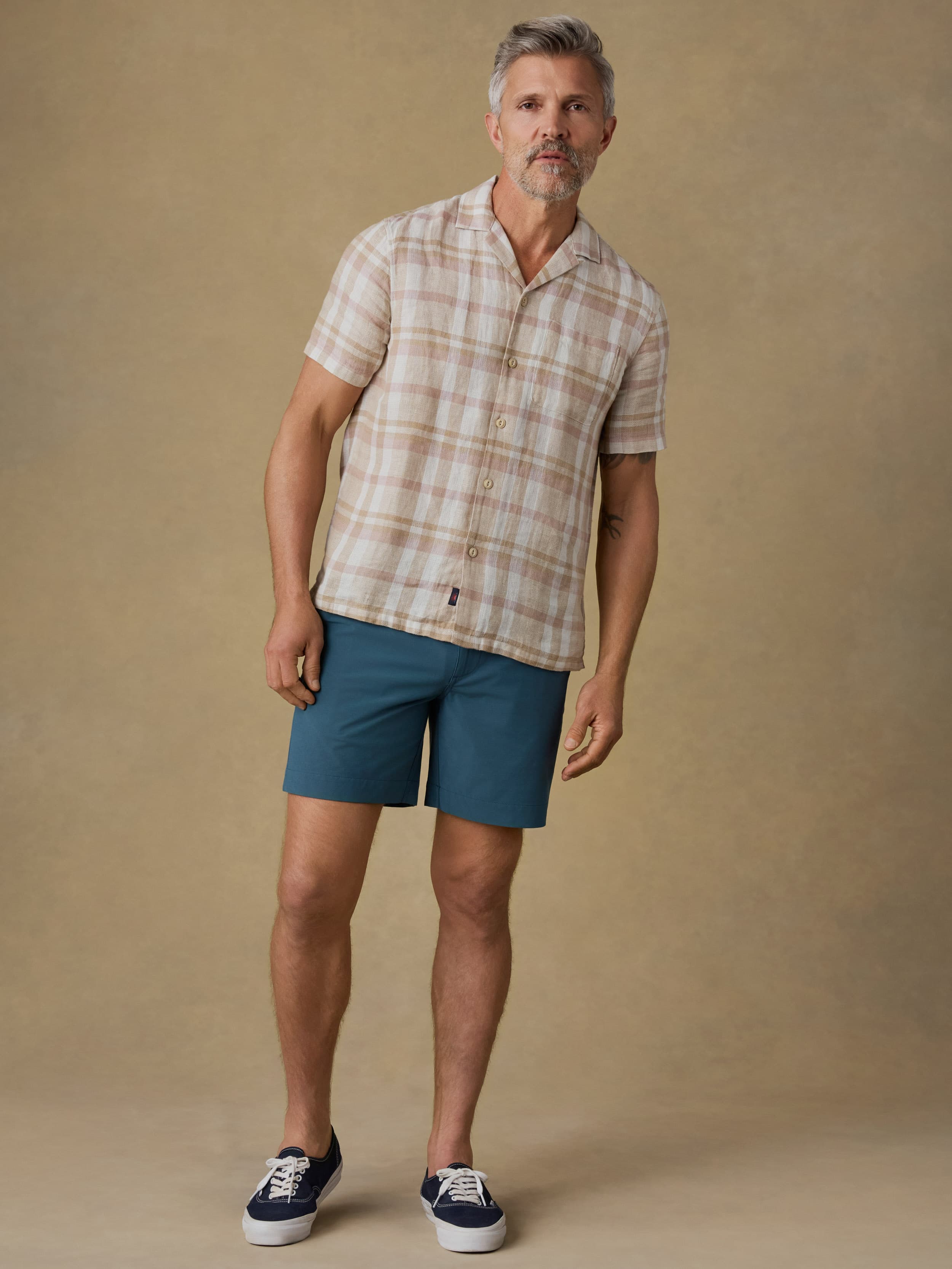 Man wearing a plaid shirt and blue shorts against a beige background