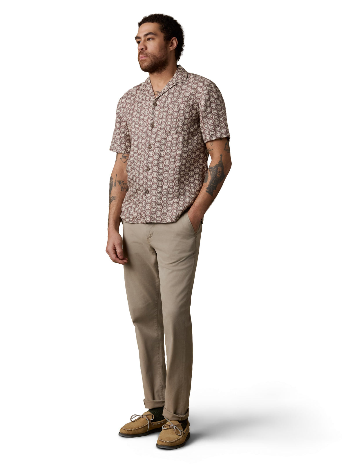 A man wearing a brown printed shirt, beige pants, and boat shoes, image 2 of 3