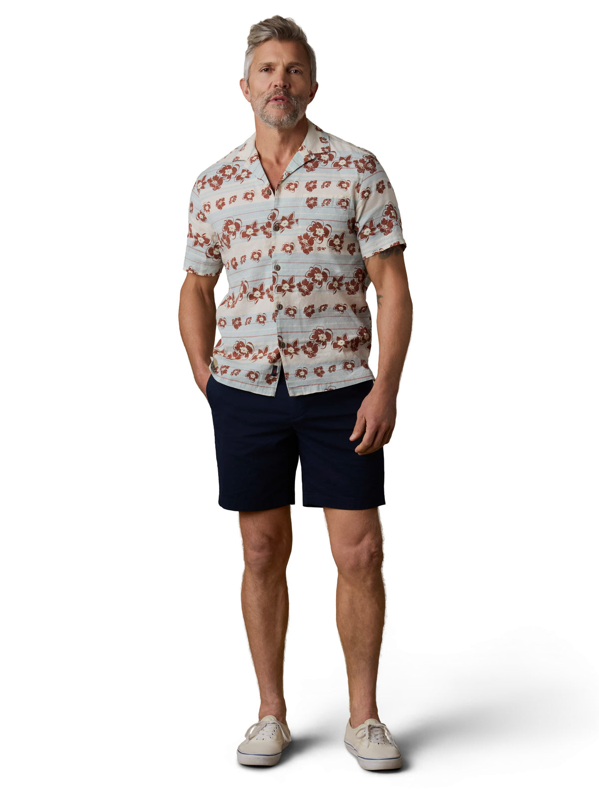 A man wearing a floral printed button up shirt, black shorts, and sneakers, image 2 of 3