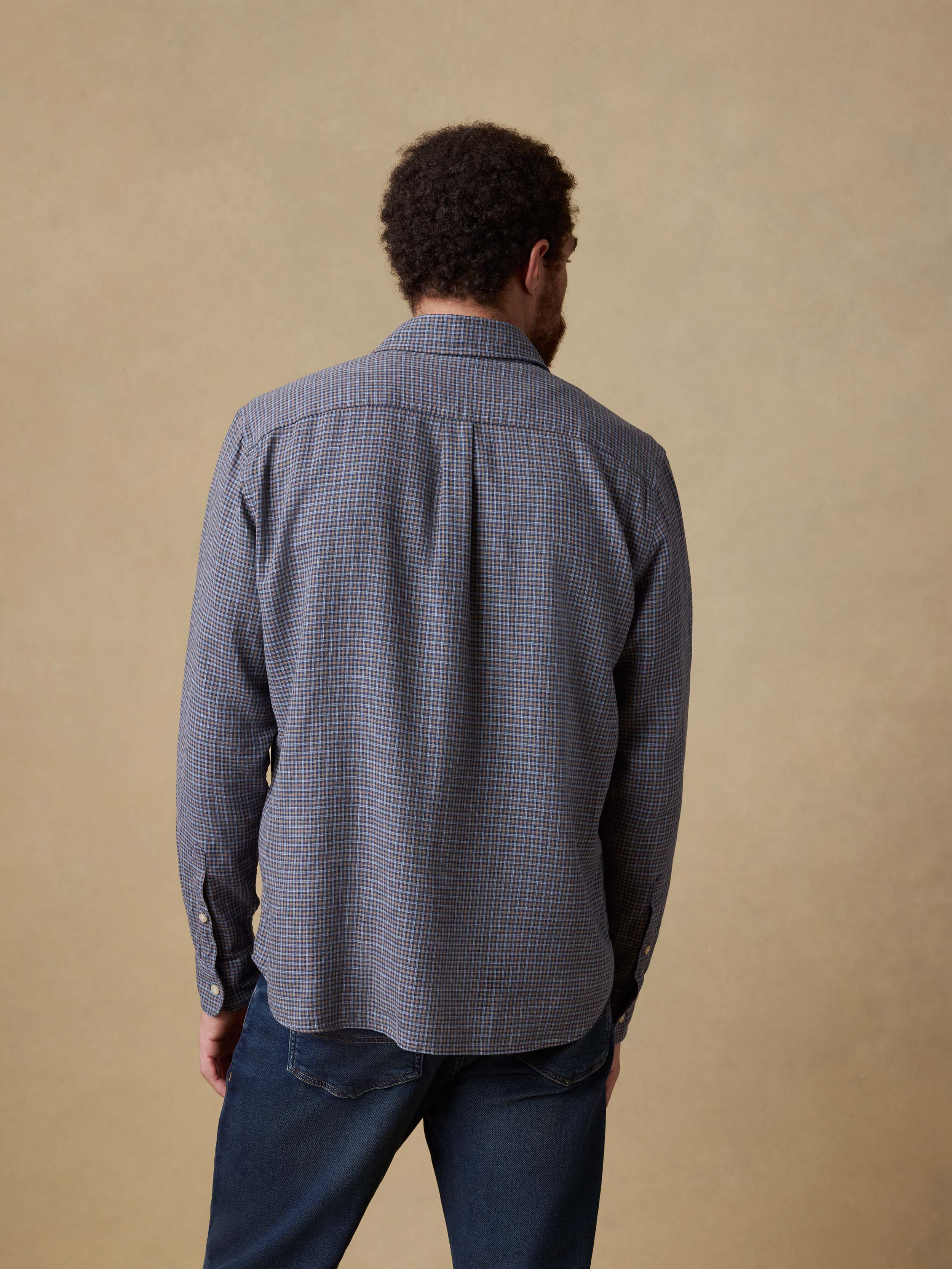 Back view of a man wearing a blue checkered shirt and blue jeans against a beige background