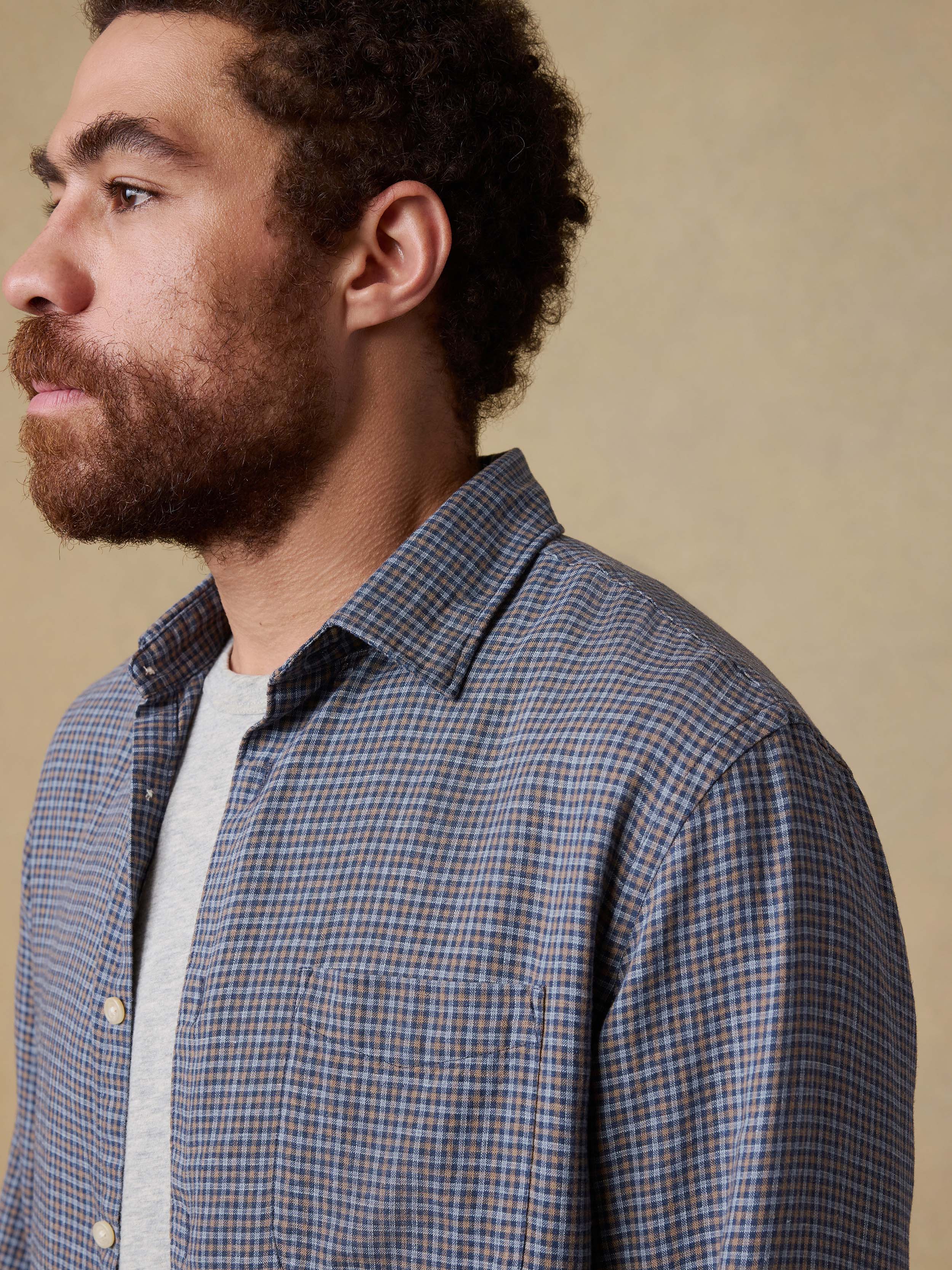 Man wearing a blue checkered shirt over a gray t-shirt against a beige background