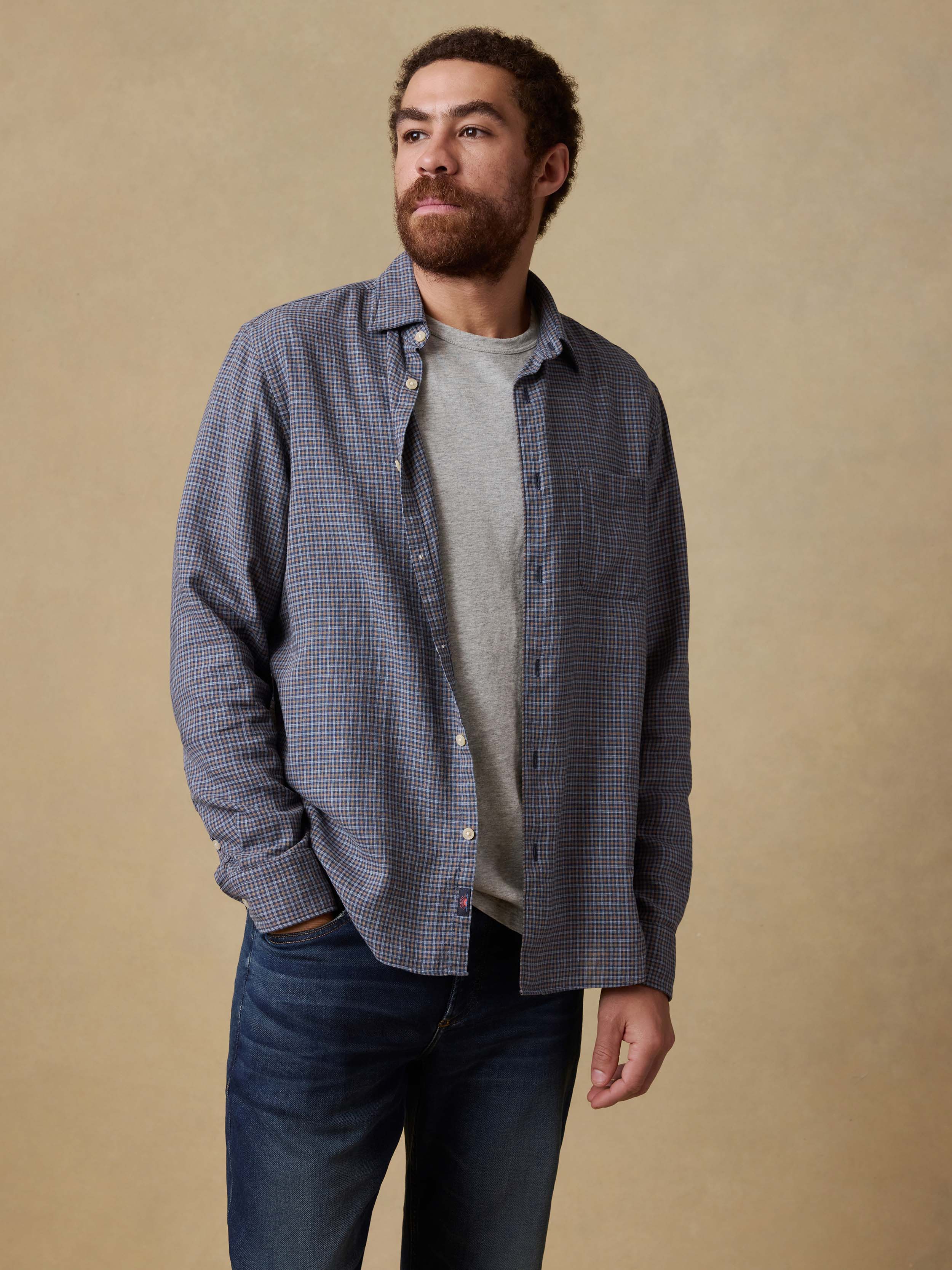 Man wearing a blue checkered shirt over a gray t-shirt and blue jeans against a beige background