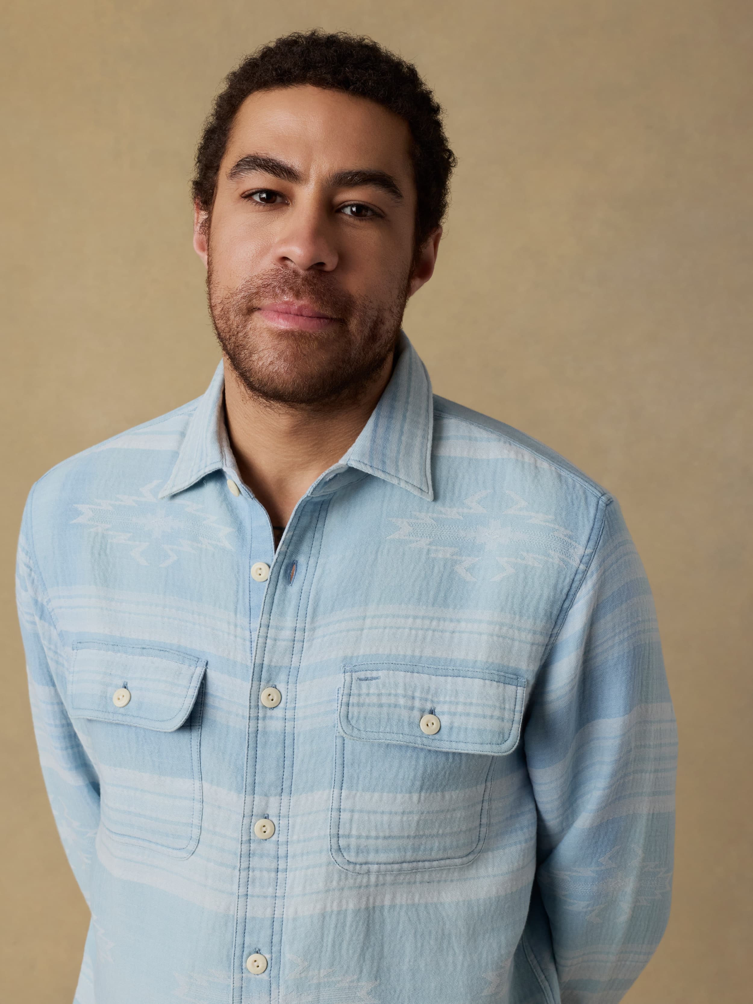 Detail shot of a man wearing a light indigo button down shirt against a beige background