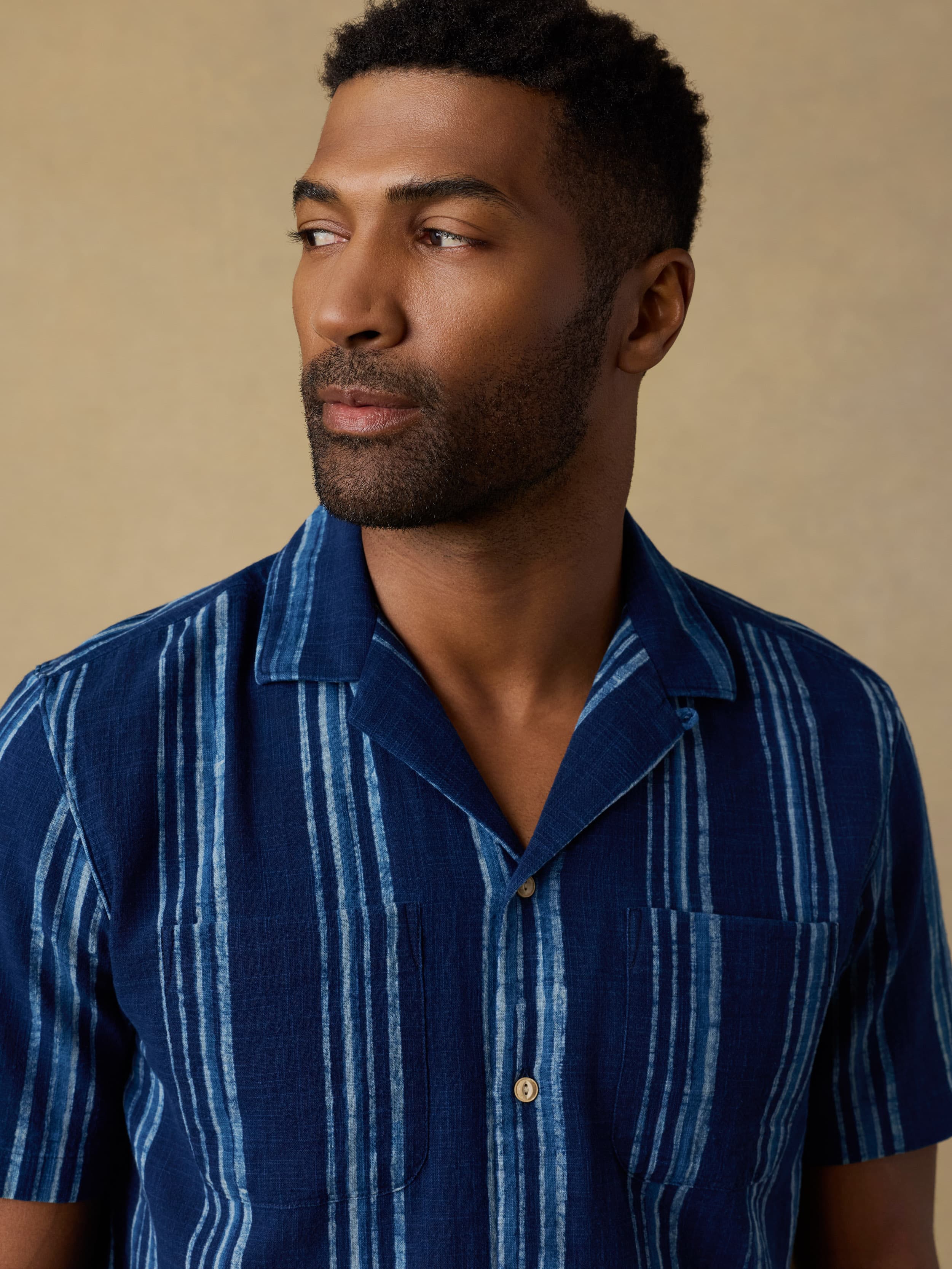 Man wearing a blue striped short sleeve button down shirt against a beige background