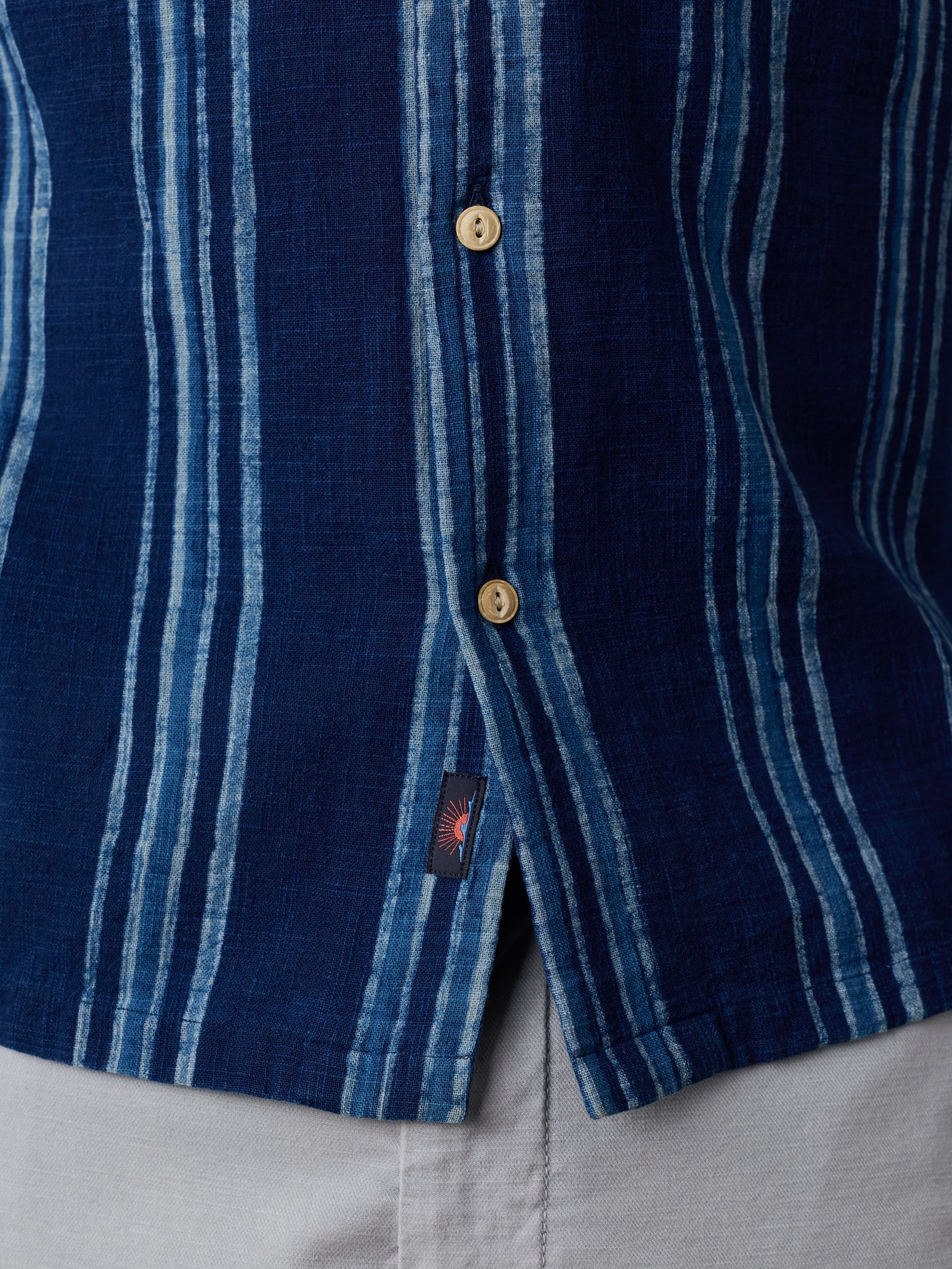 Close up of a blue striped short sleeve button down shirt with a visible Faherty brand logo near the hem
