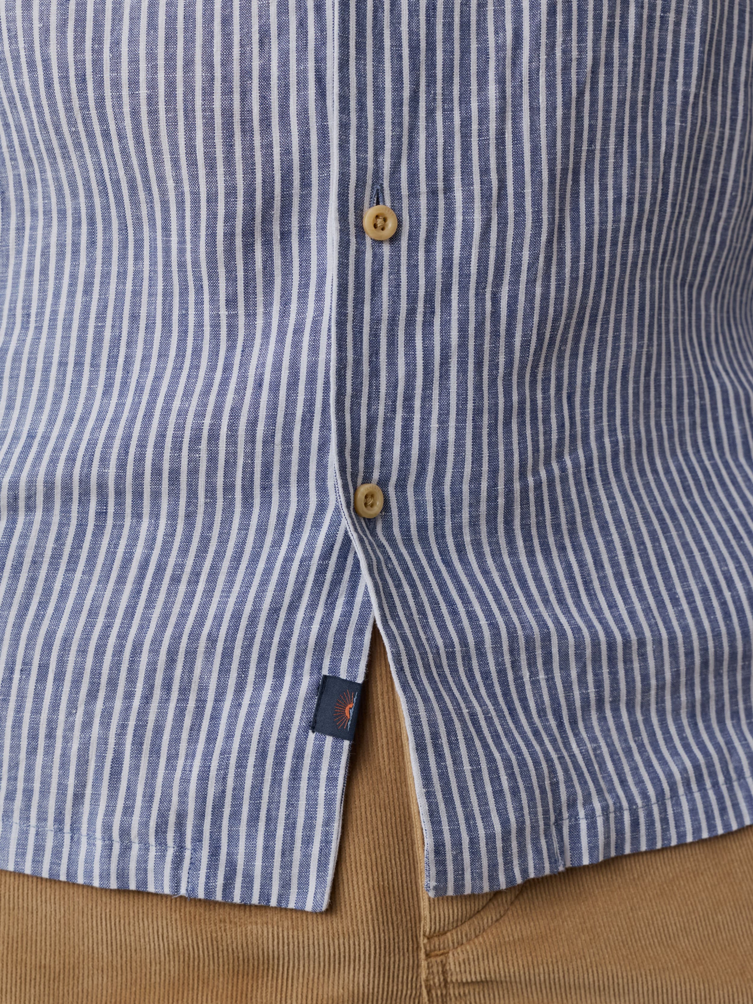 Close-up of a blue and white striped shirt with a button with a Faherty brand label near the hem