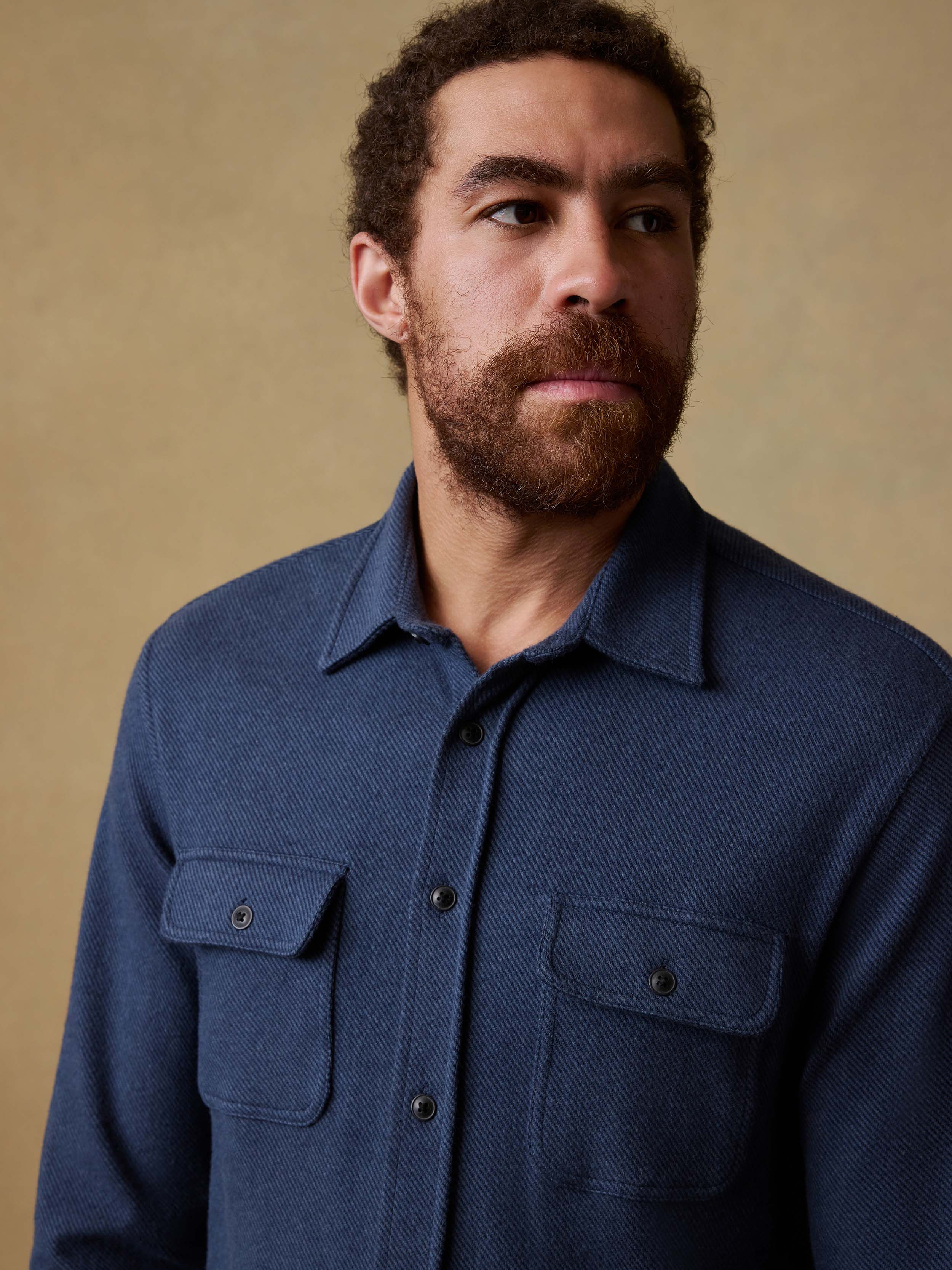 Man wearing a navy blue button down shirt against a beige background