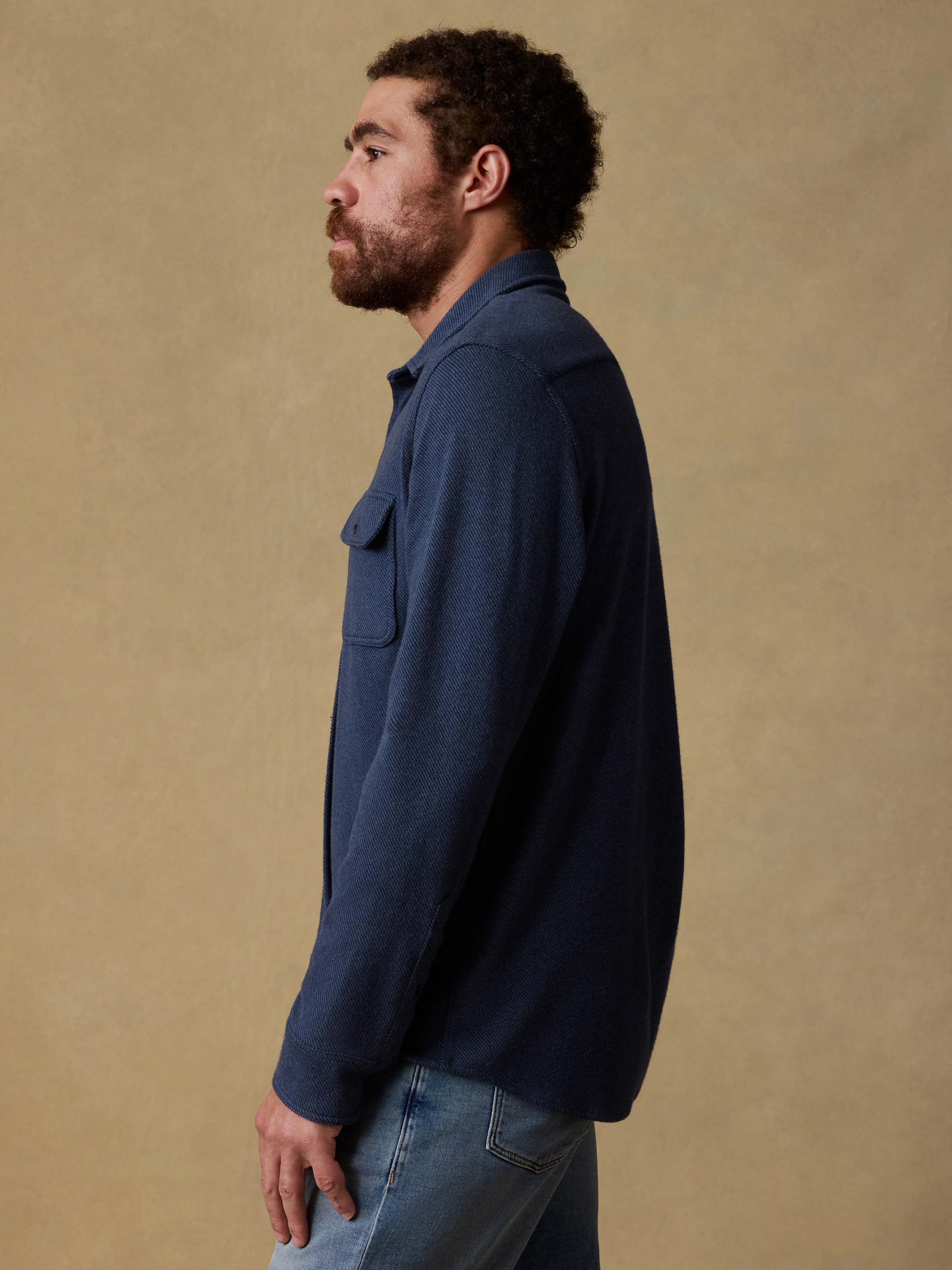 Man wearing a navy blue button down shirt and jeans against a beige background