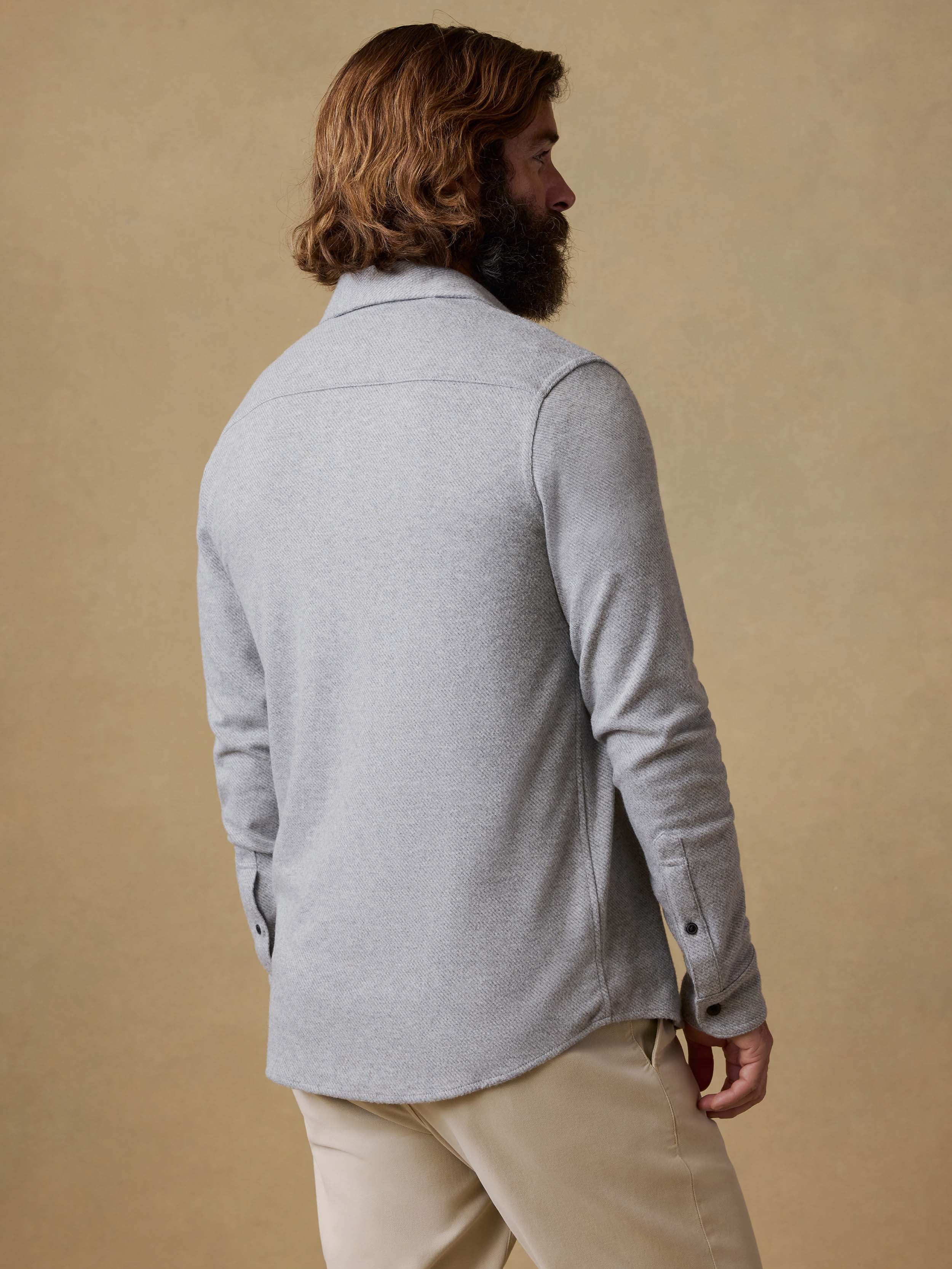 Back view of a man wearing a gray long-sleeve shirt and beige pants against a beige background