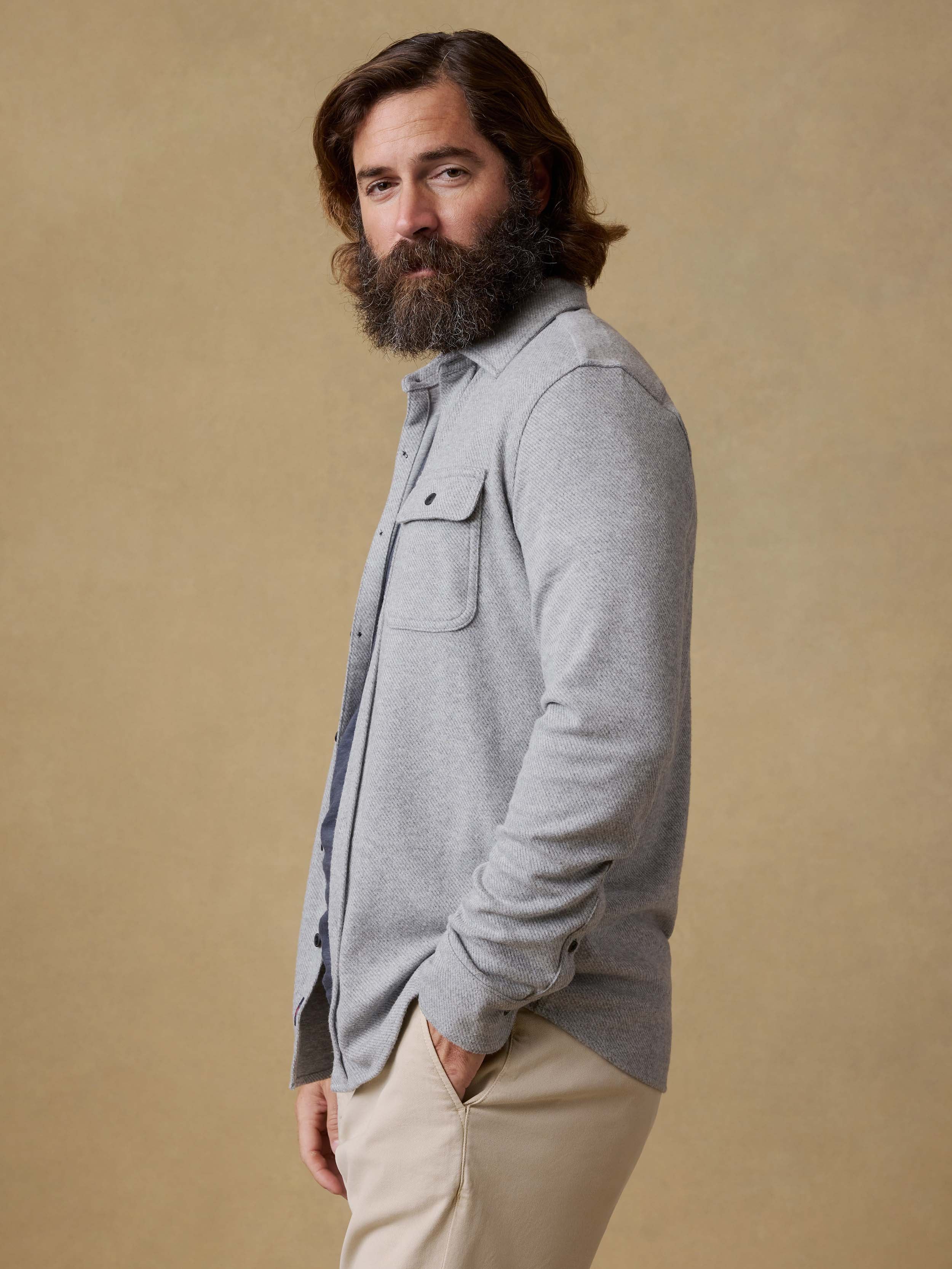 Man wearing a gray long-sleeve shirt and beige pants against a beige background