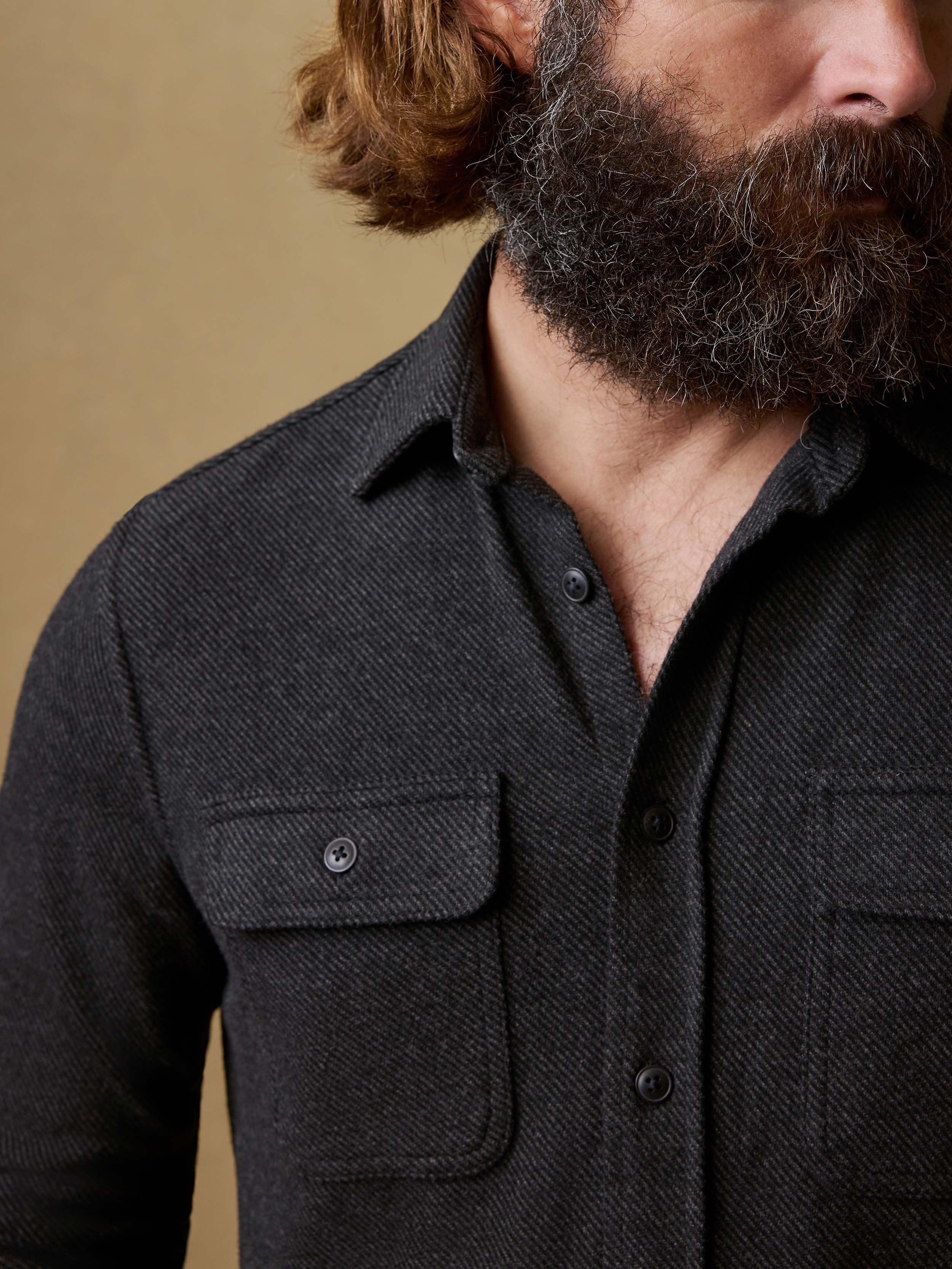 Detail shot of a man wearing a black button down shirt against a beige background