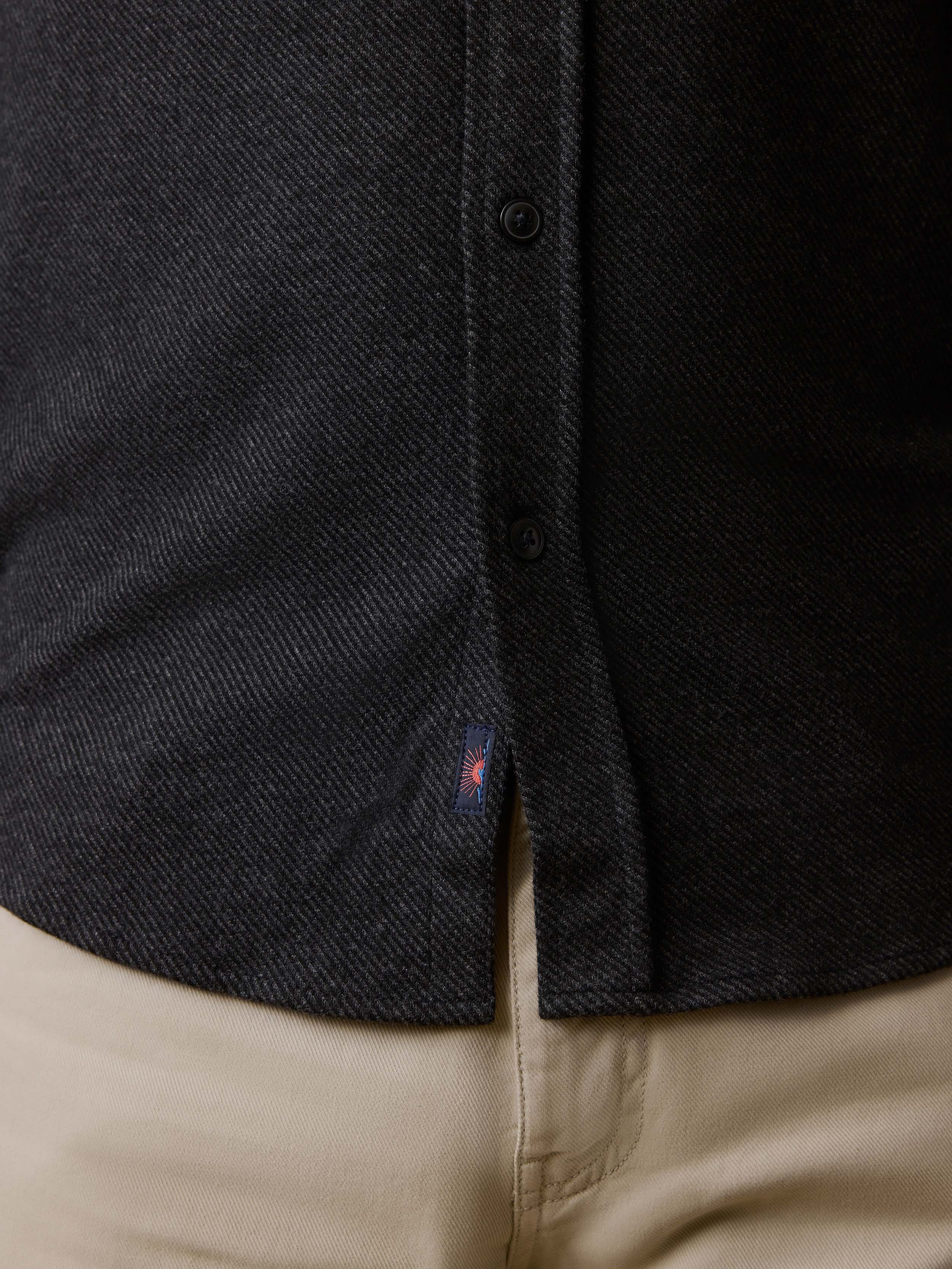 Detail shot of a man wearing a black button down shirt with visible Faherty brand logo and beige pants