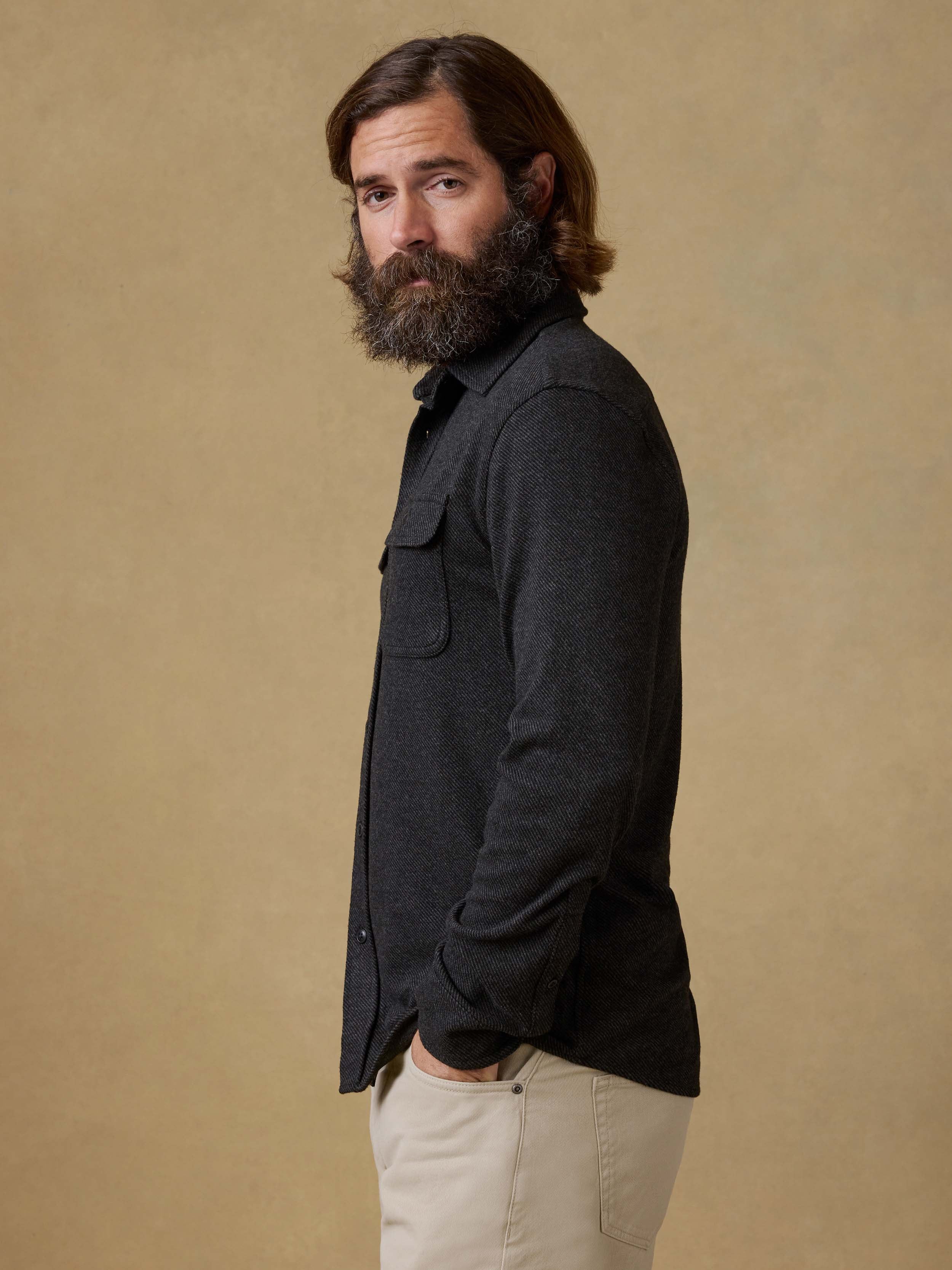 Man wearing a black button down shirt with beige pants against a beige background