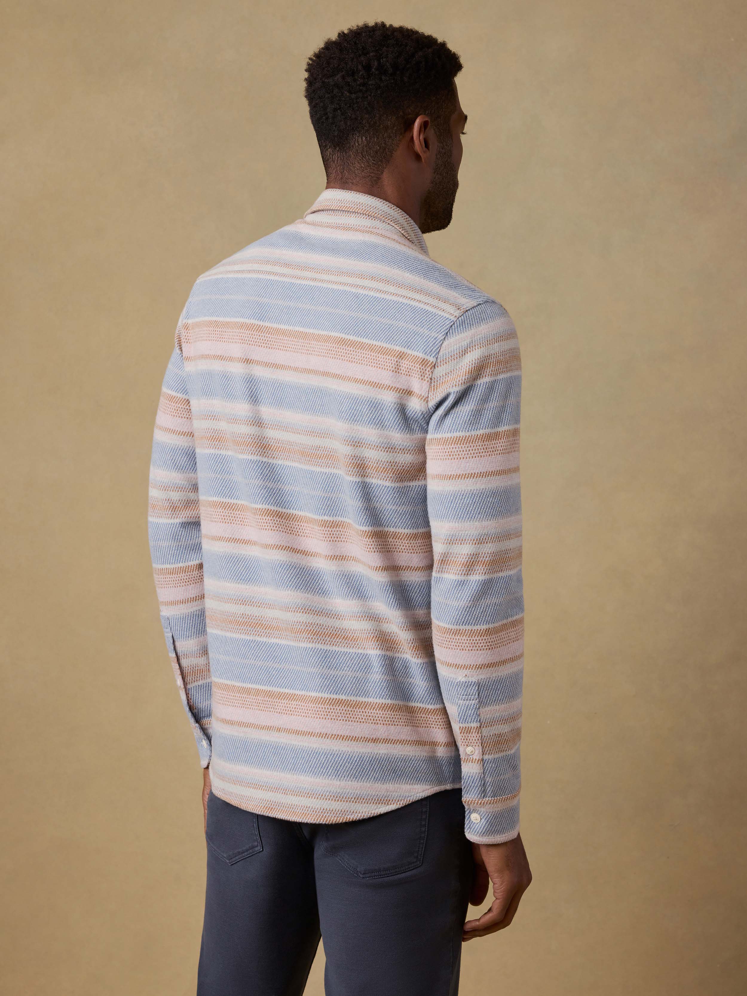 Back view of a man wearing a striped long-sleeve shirt against a beige background