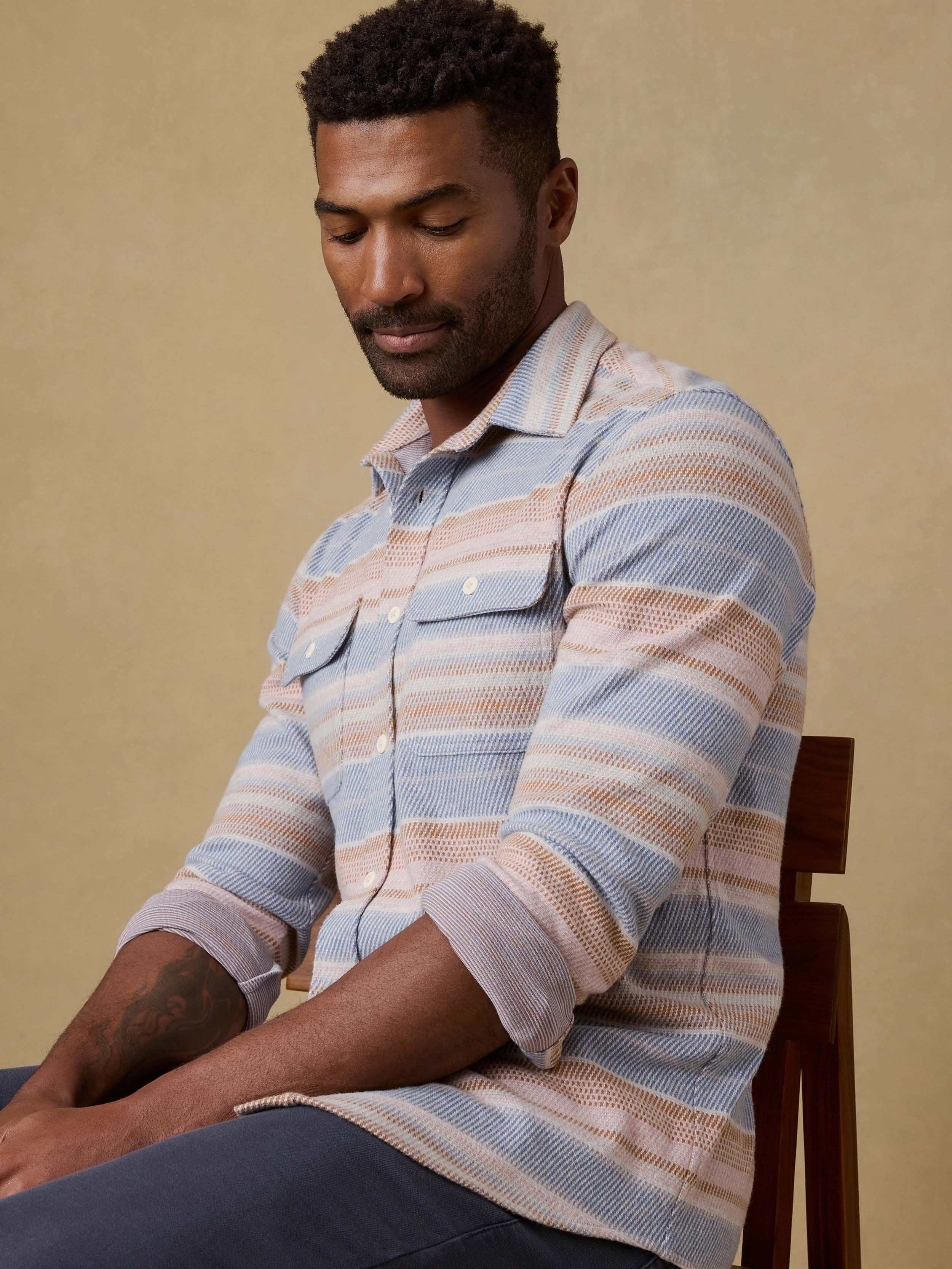 Man wearing a striped shirt sitting on a chair against a beige background