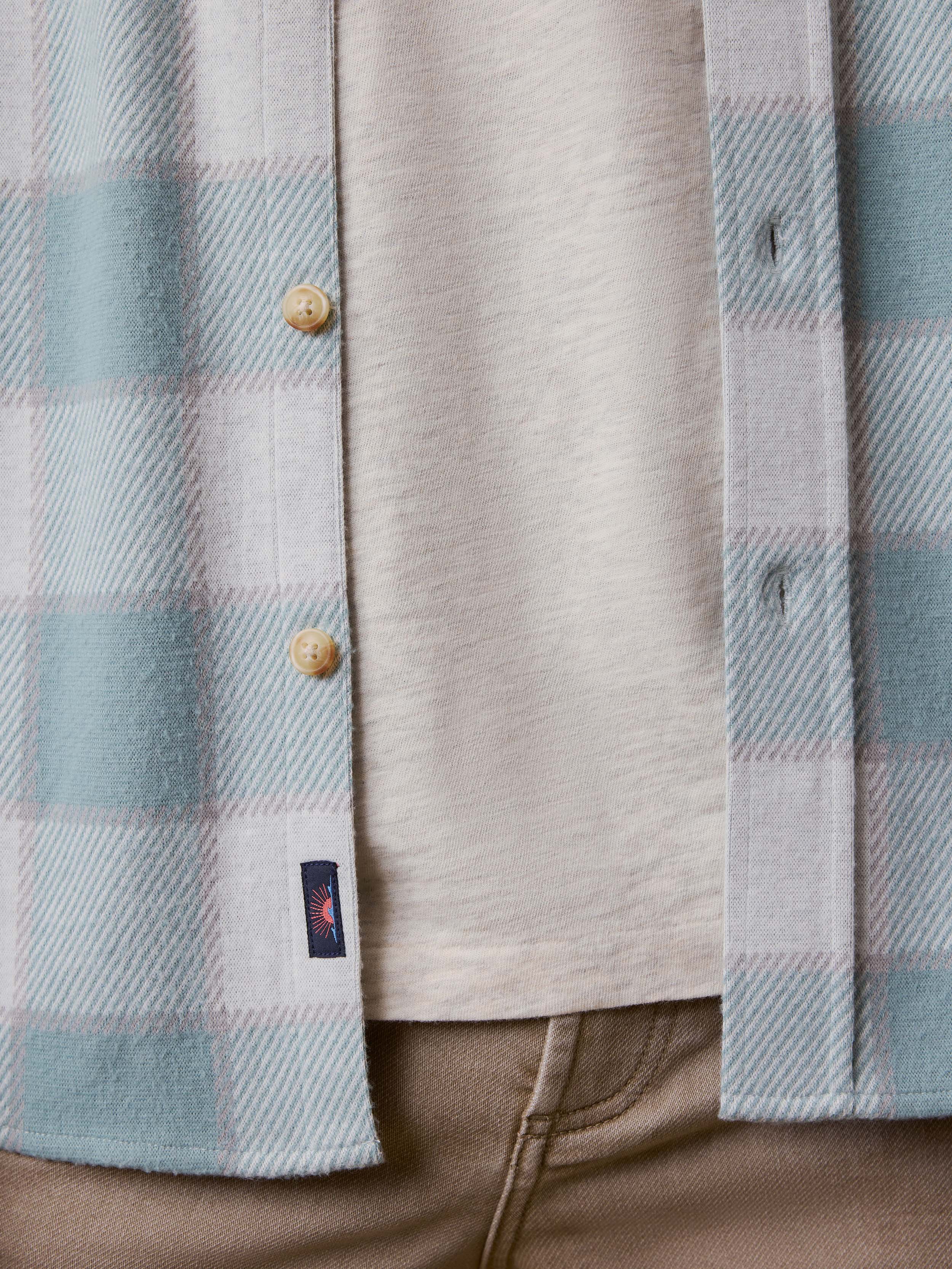 Close-up of a plaid shirt with a Faherty brand logo at the hem
