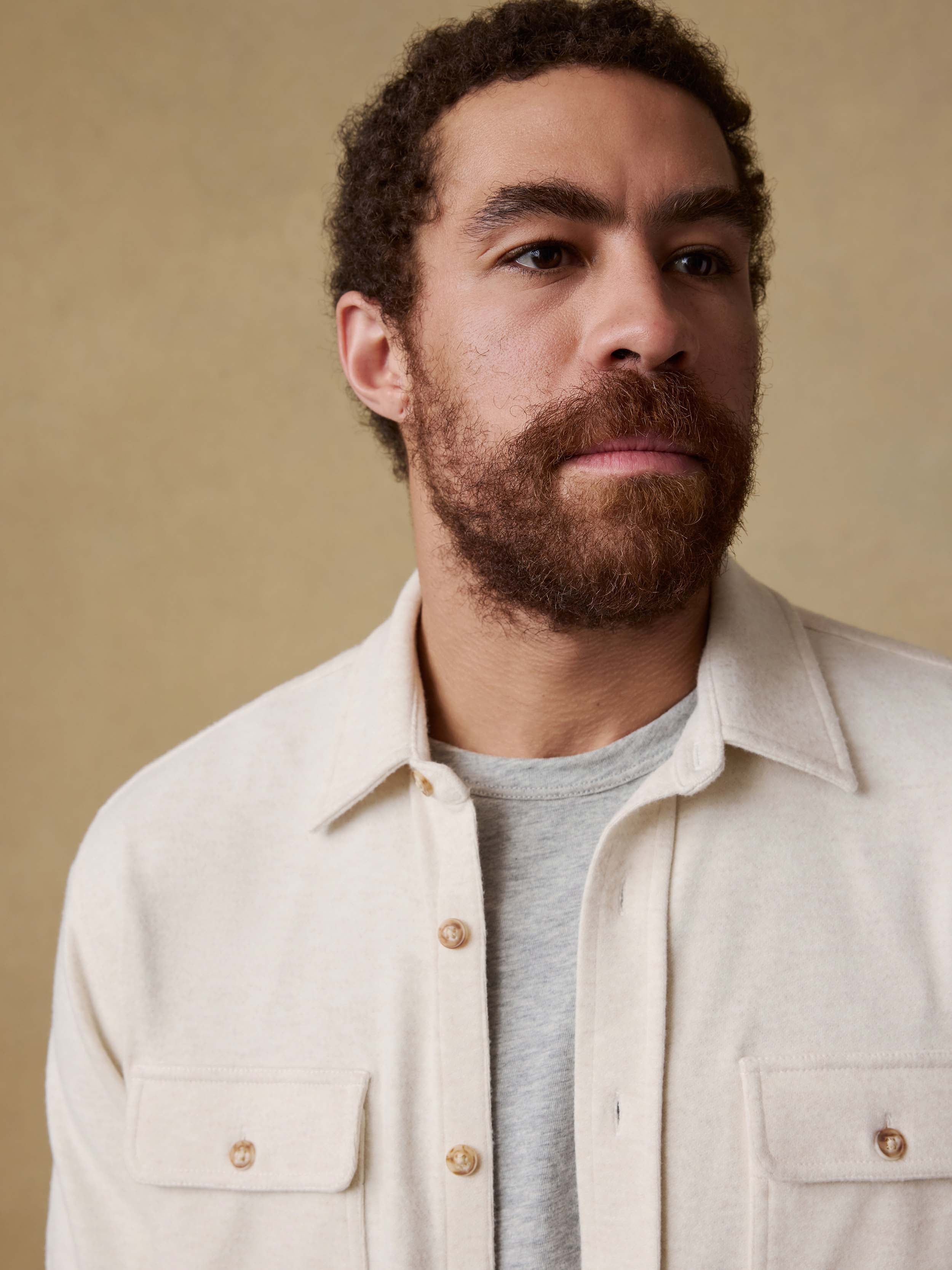 Detail shot of a man wearing an off white button up shirt over a gray t-shirt against a beige background