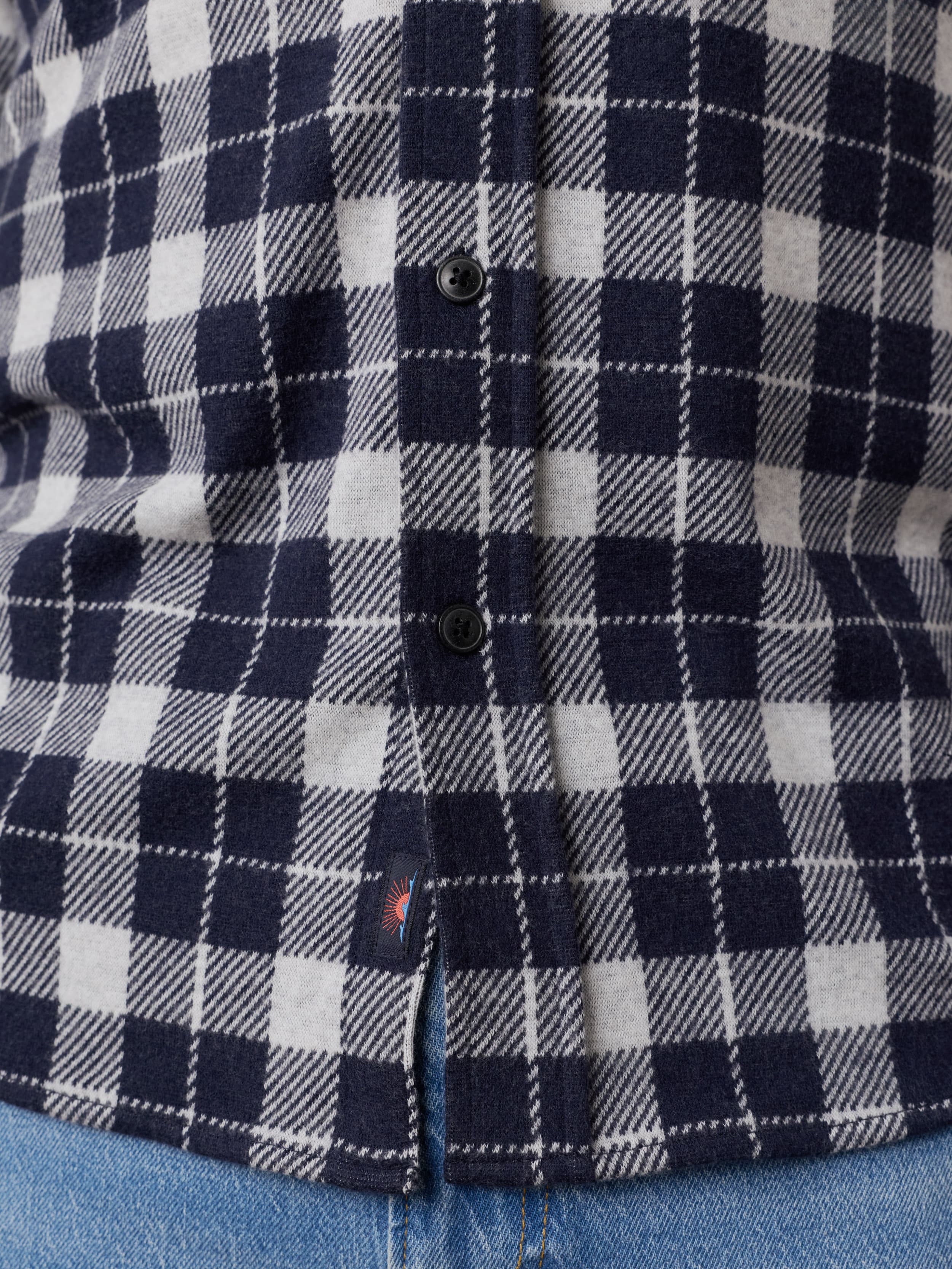 Close-up of a navy and white plaid long sleeve button up shirt with a Faherty brand logo near the hem.