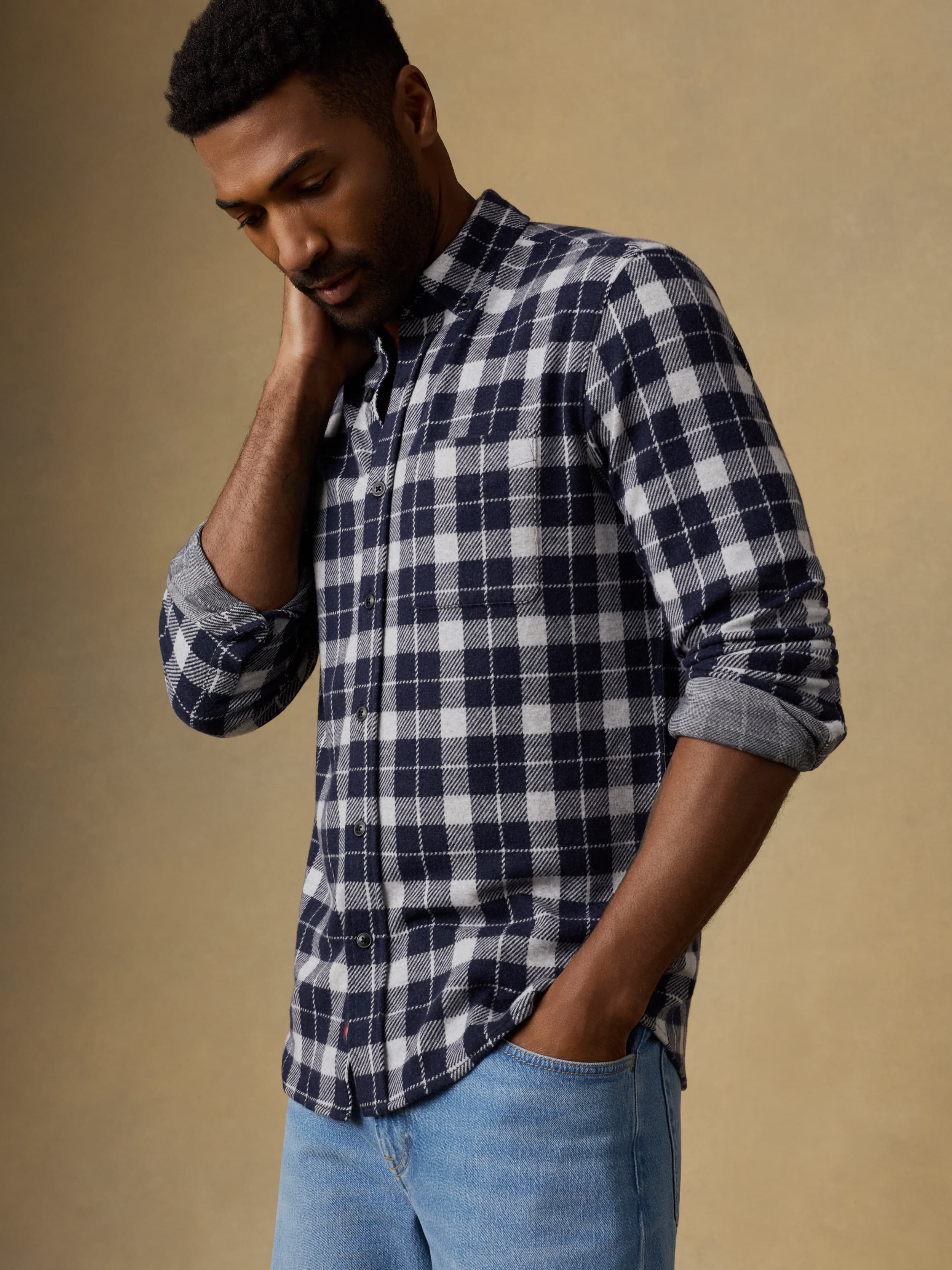 Man wearing a navy and white checkered long sleeve button up shirt and blue jeans against a beige background