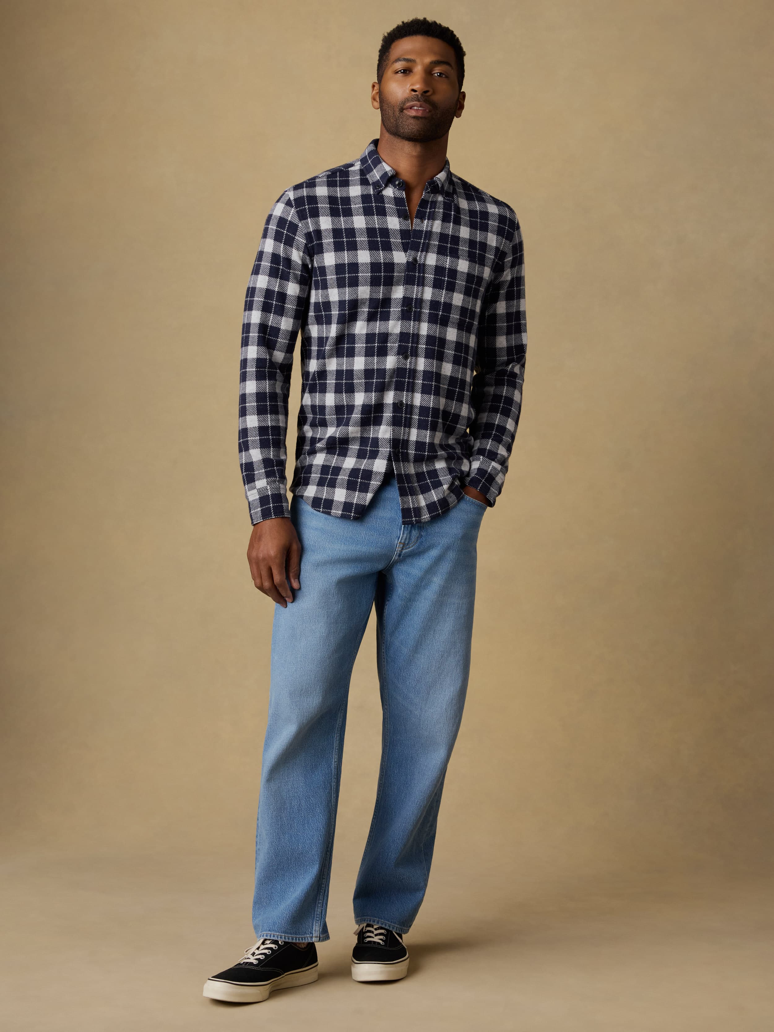 Man wearing a navy and white checkered long sleeve button up shirt and blue jeans against a beige background