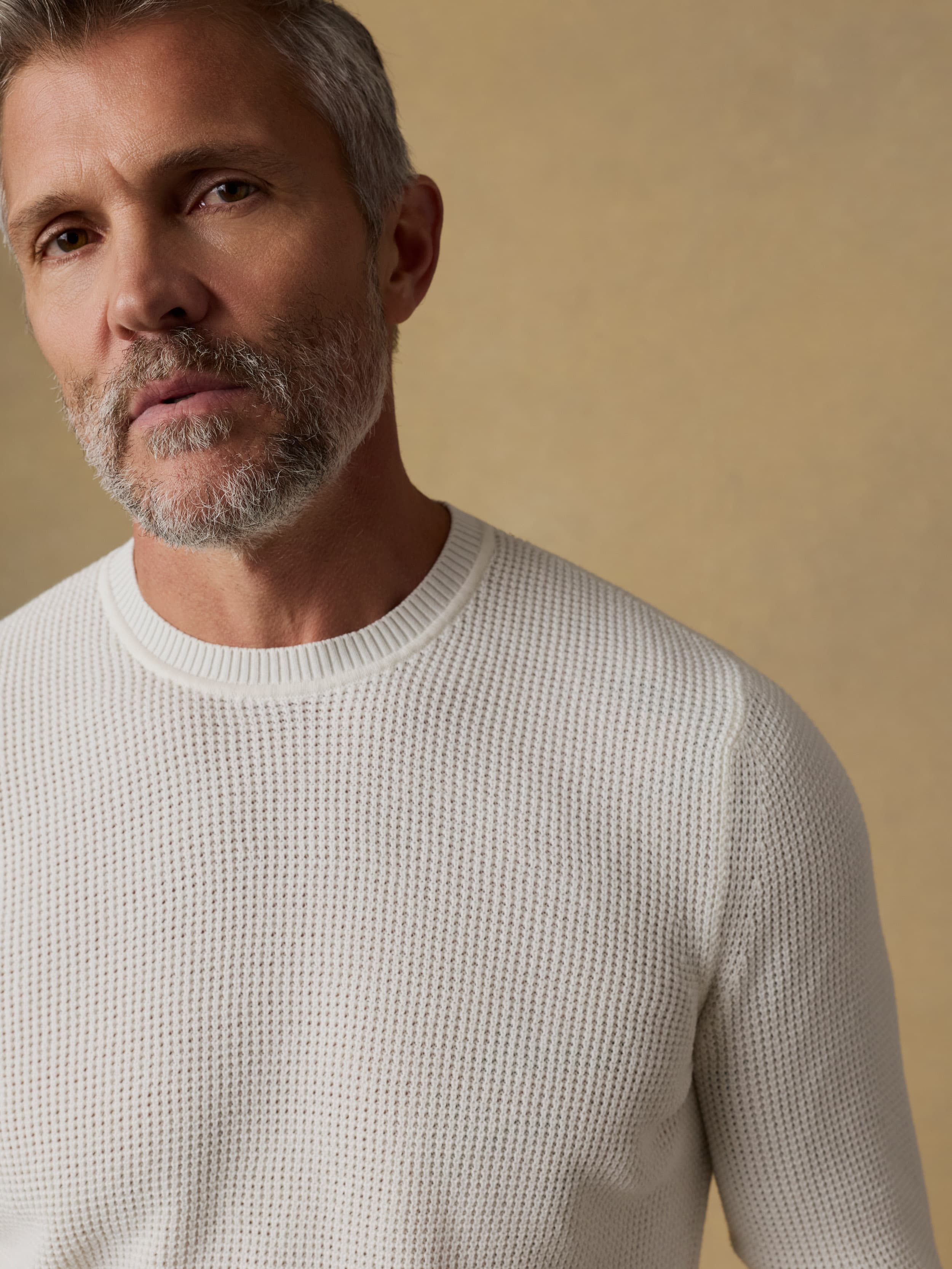 Close up of a man wearing a white crewneck sweater against a beige background