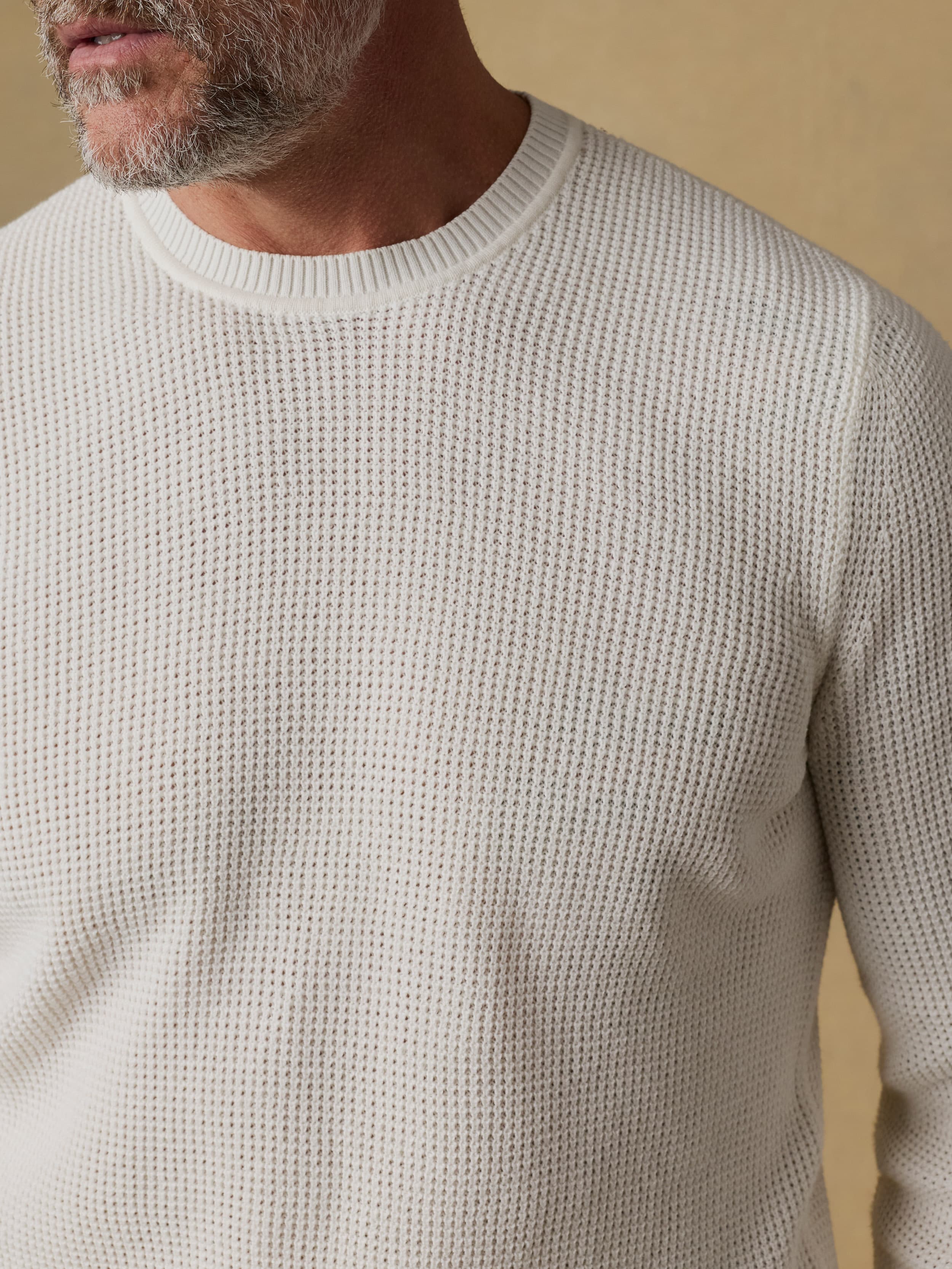 Close up shot of a man wearing a white crewneck sweater against a beige background