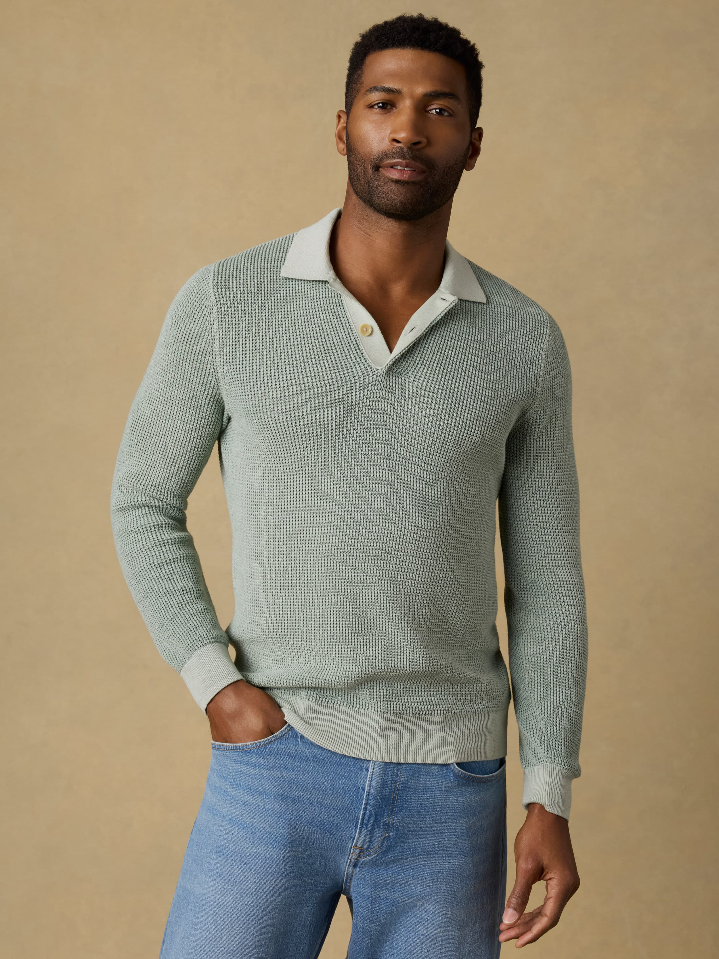 Man wearing a light green polo sweater with blue jeans on a beige background