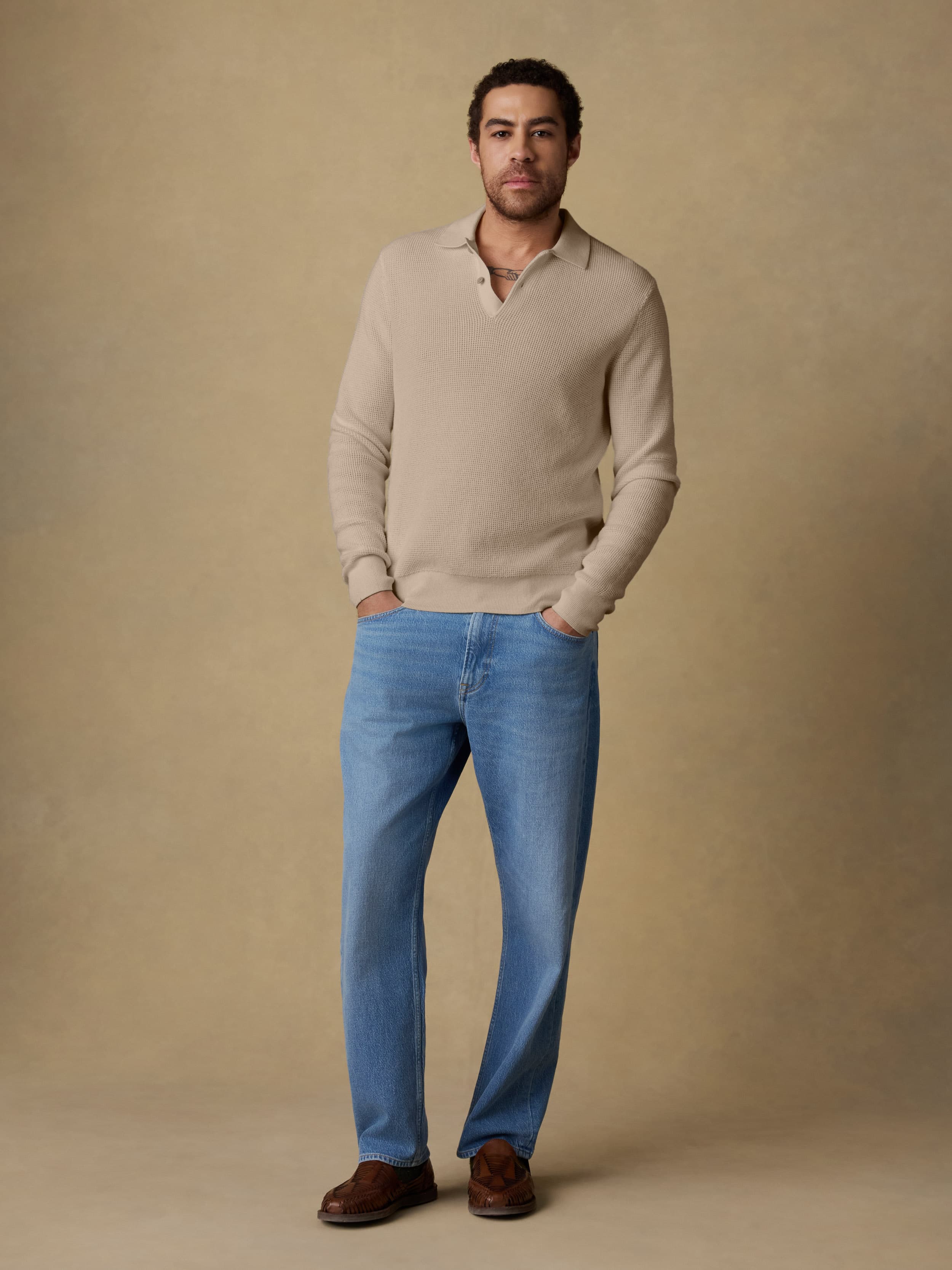 Man wearing a beige sweater and blue jeans against a beige background